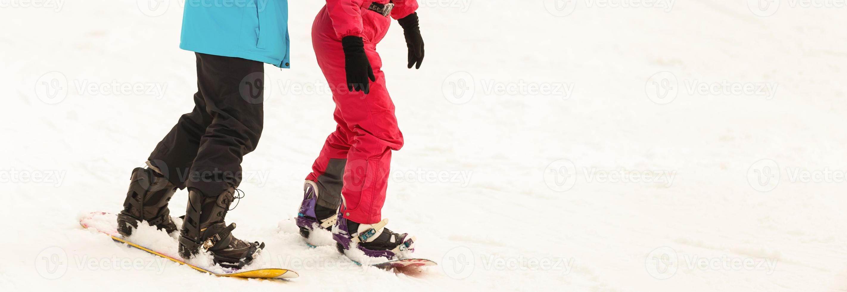 Pair of snowboarders on top of a ski slope at winter resort downhill on a sunny day. photo