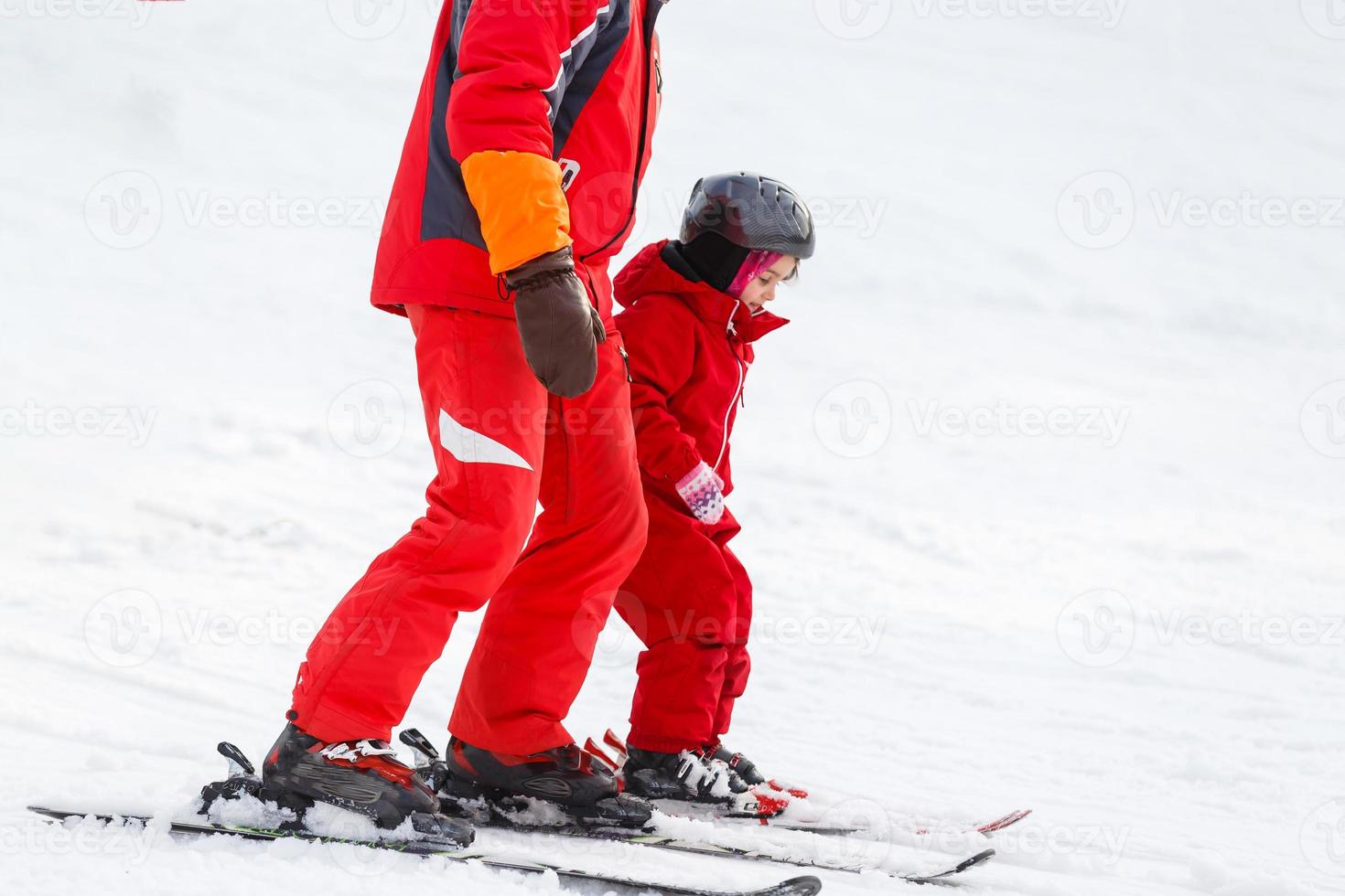 Professional ski instructor is teaching a child to ski on a sunny day on a mountain slope resort with sun and snow. Family and children active vacation. photo
