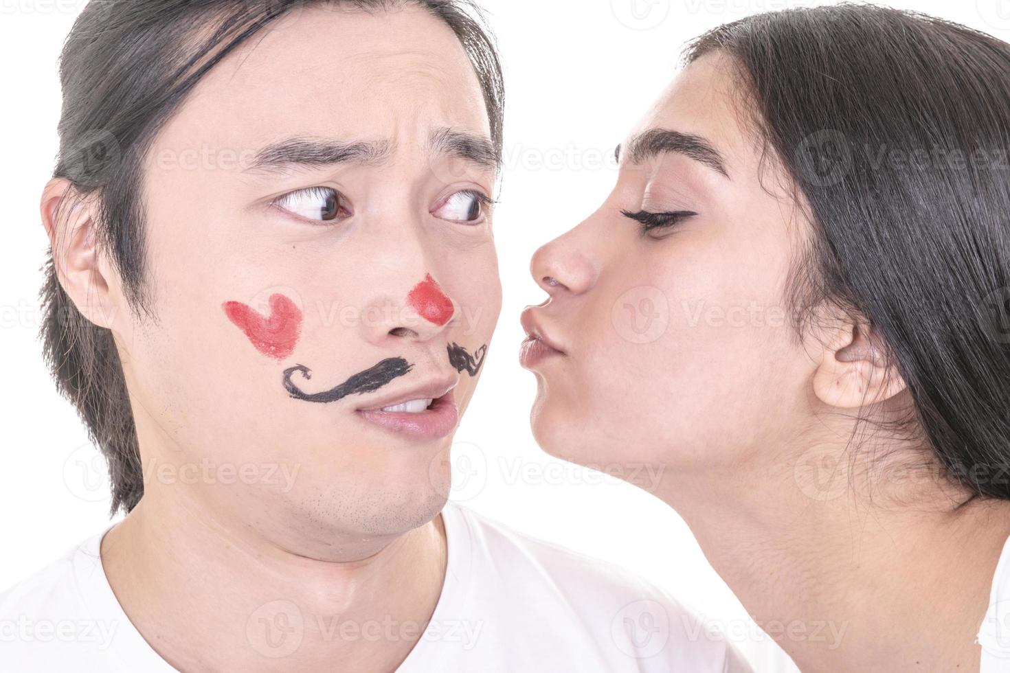 Mixed couple having fun. Arabic female model giving kiss to Asian male model who have drowned mustaches and heart on his face. isolated on white background. photo