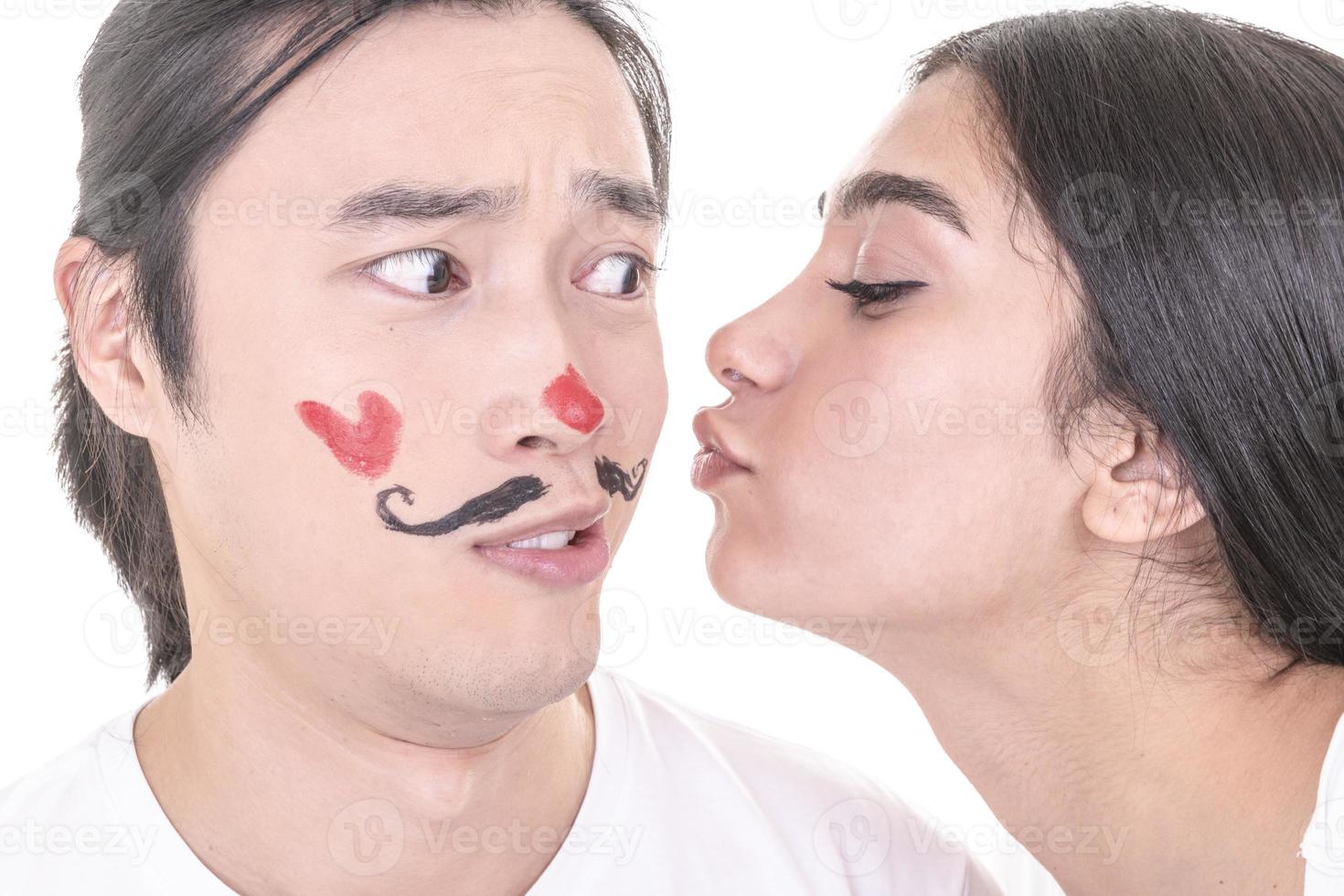 pareja mixta divirtiéndose. modelo femenino árabe dando beso a modelo masculino asiático que ha ahogado bigotes y corazón en su cara. aislado sobre fondo blanco. foto