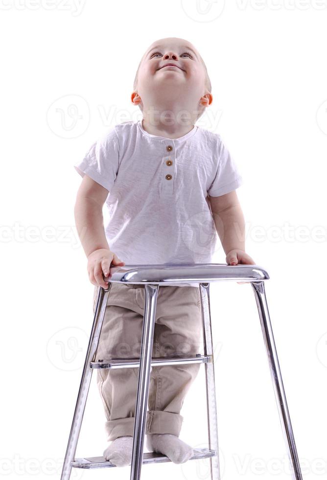 niño sube a una silla de escalera. el comienzo de un concepto de carrera. niño divertido aislado sobre fondo blanco. foto