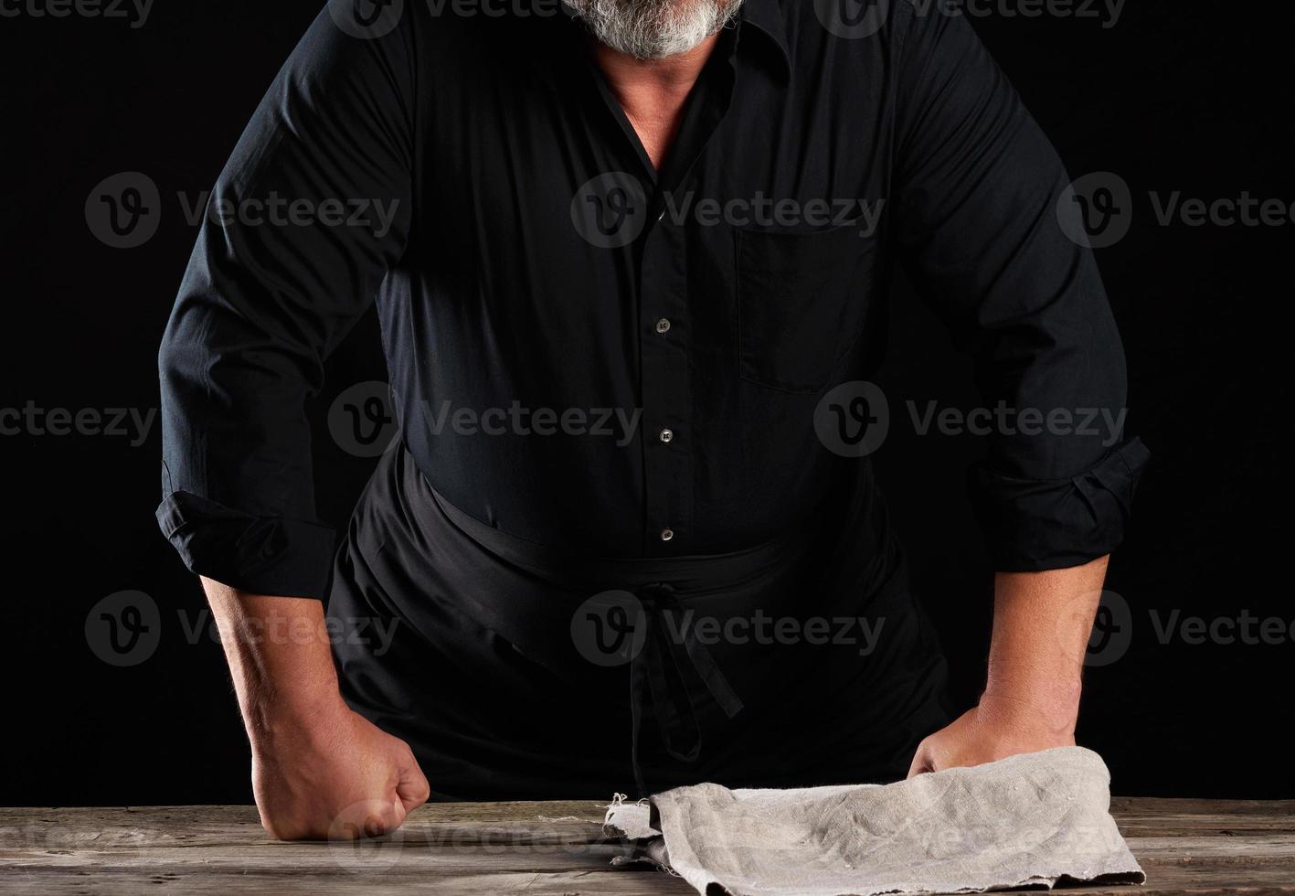 chef man in black uniform bent over a wooden table and rested his fists photo