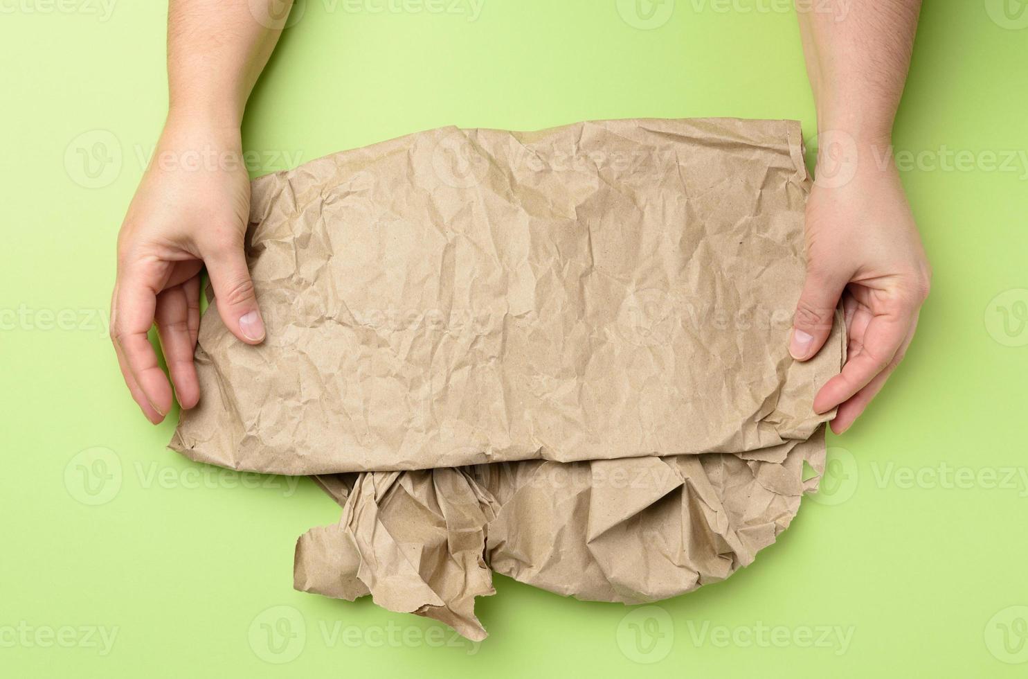 two hand holds piece of crumpled brown paper on a green background photo