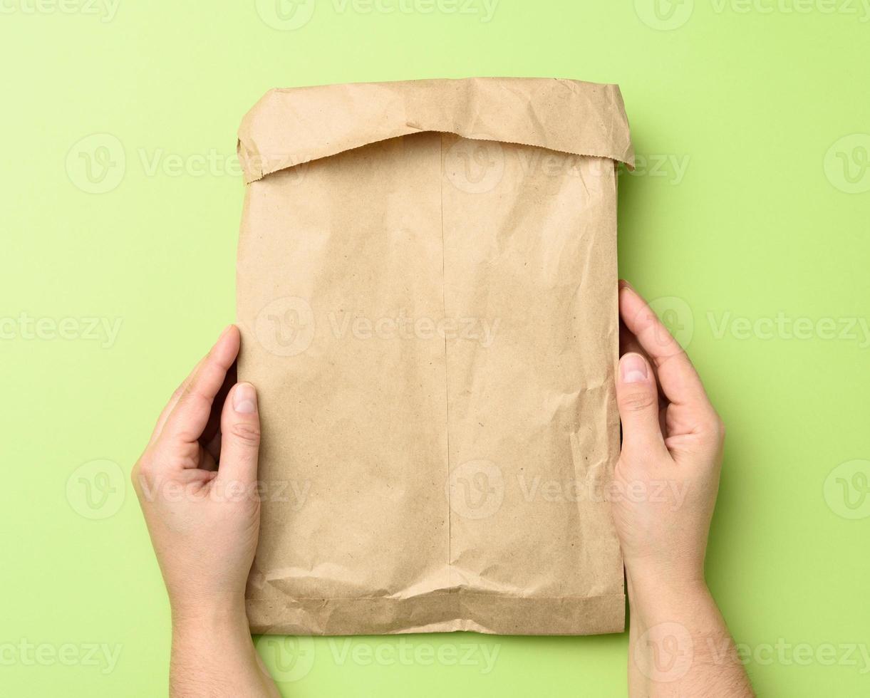 two hands holding a paper bag of brown kraft paper ona green background photo