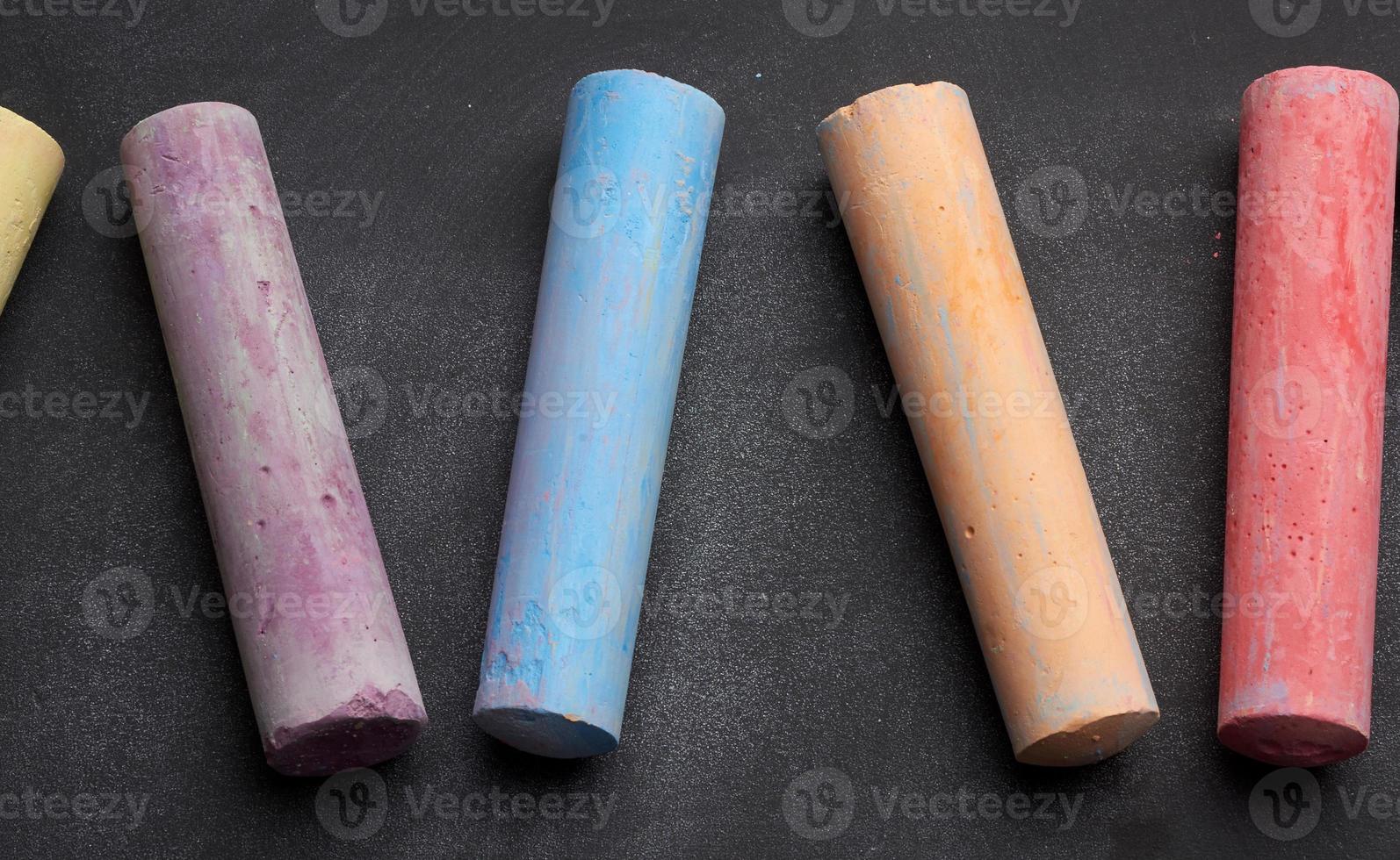 multicolored chalks on lie on empty black chalk board, top view photo