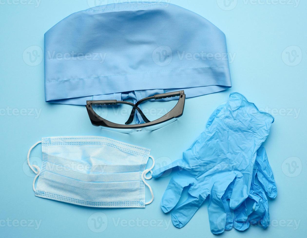 textile blue cap, disposable medical mask, pair of gloves and plastic glasses photo