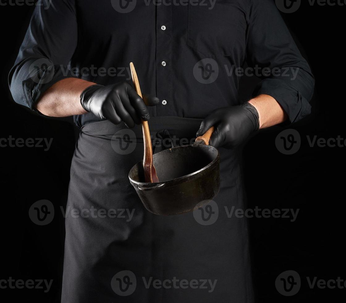 cocinero masculino con uniforme negro y guantes de látex sostiene una sartén redonda vacía de hierro fundido negro vintage foto