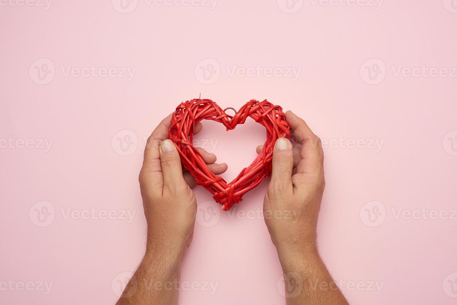 two male hands holding a red wicker heart on a pink background photo