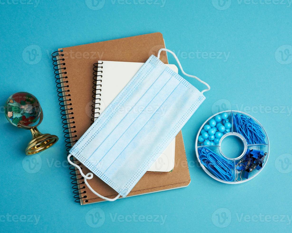 disposable medical face mask and spiral paper notebook, stationery on blue background photo