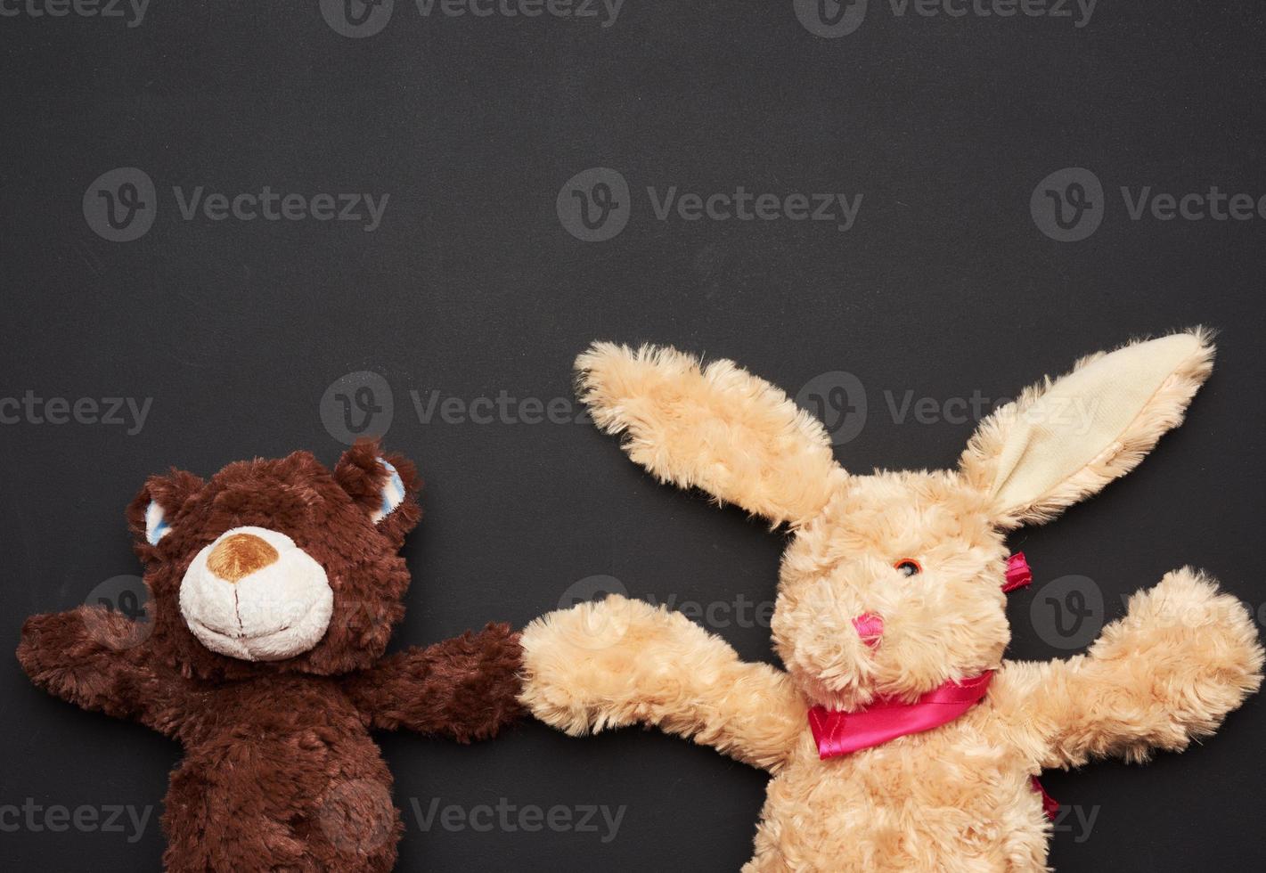 beige plush rabbit toy with long ears and a brown bear on a black background photo