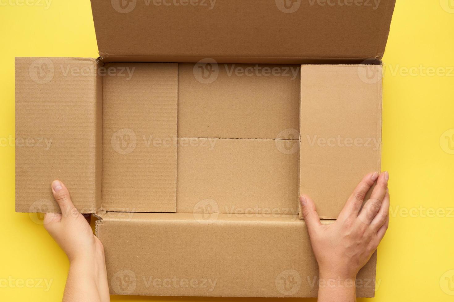female hands are holding an empty open box of brown cardboard, top view photo