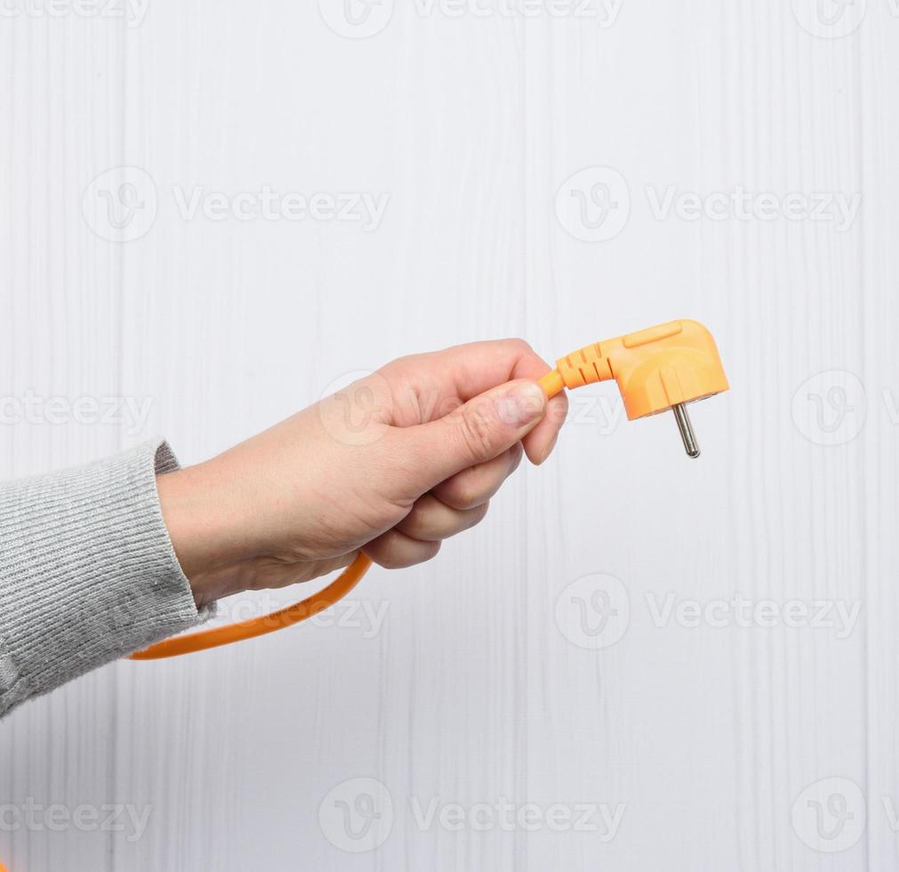 mano femenina sostiene cable naranja con enchufe para enchufe foto