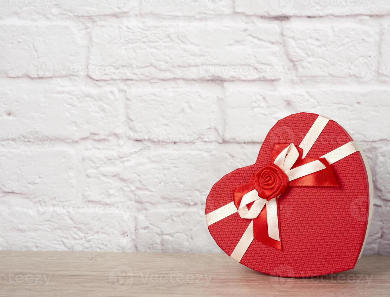 Heart shaped cardboard box with gifts on white brick wall background photo