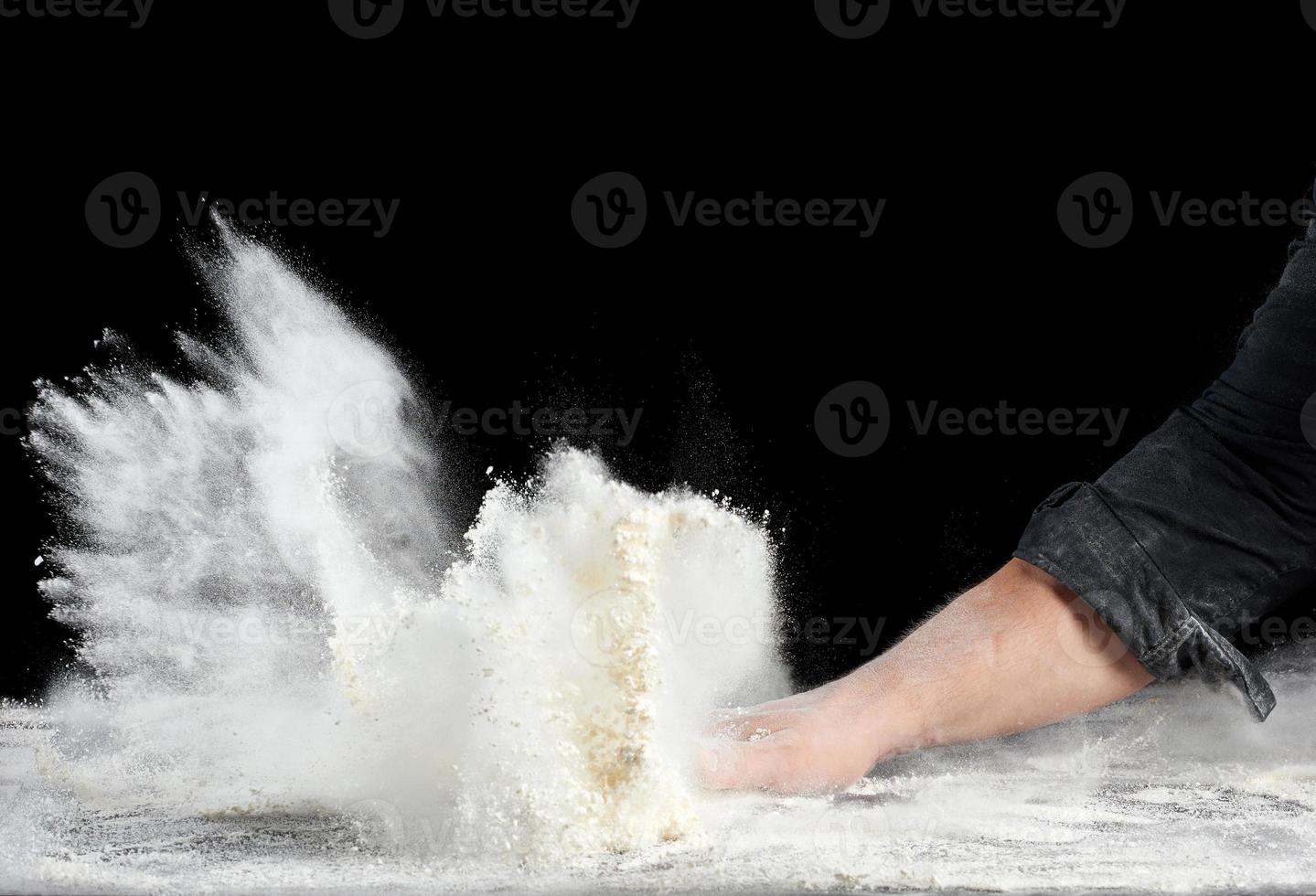 chef in black uniform sprinkles white wheat flour in different directions, product scatters dust photo