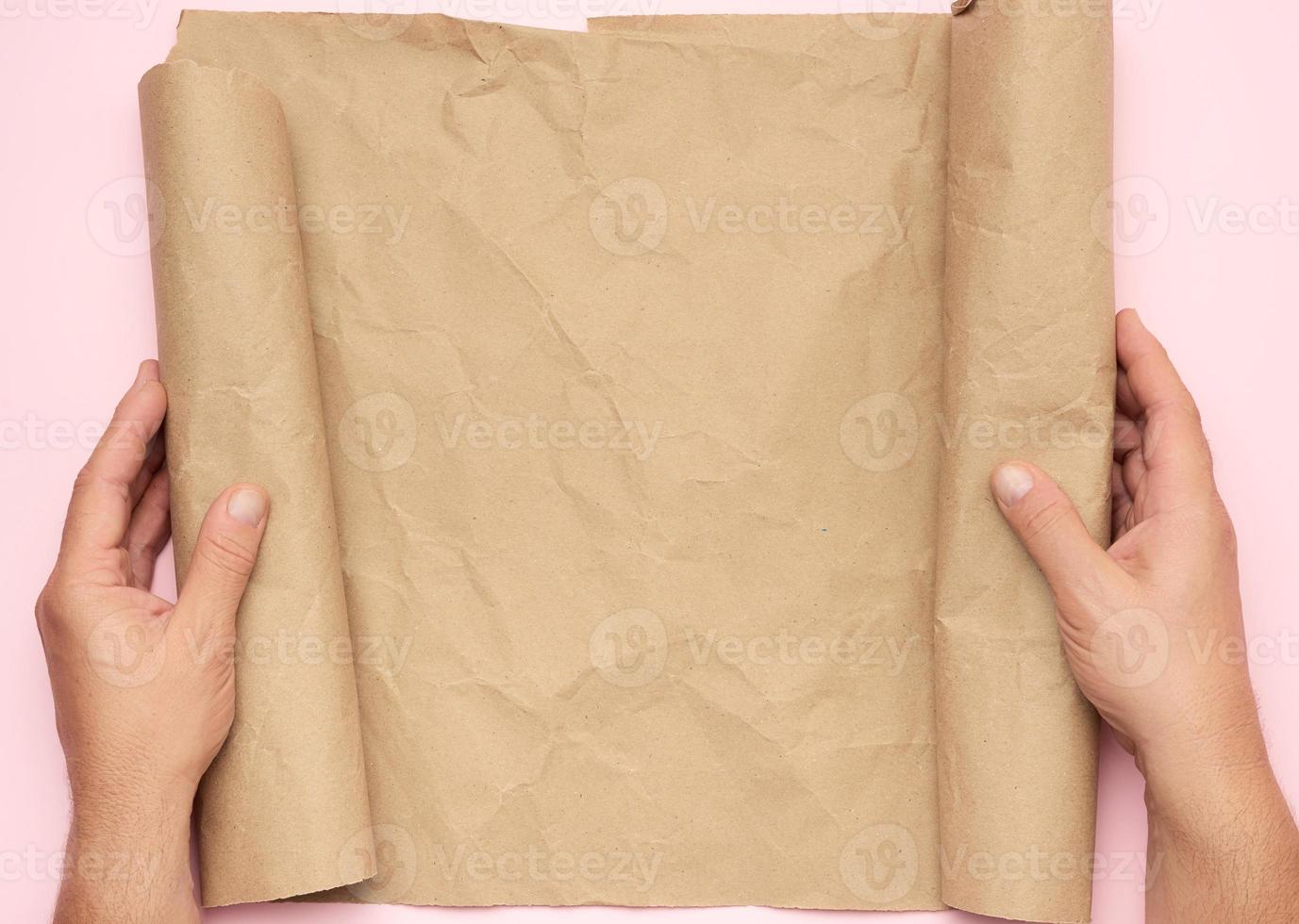 two male hands hold a roll of brown paper on a pink background photo