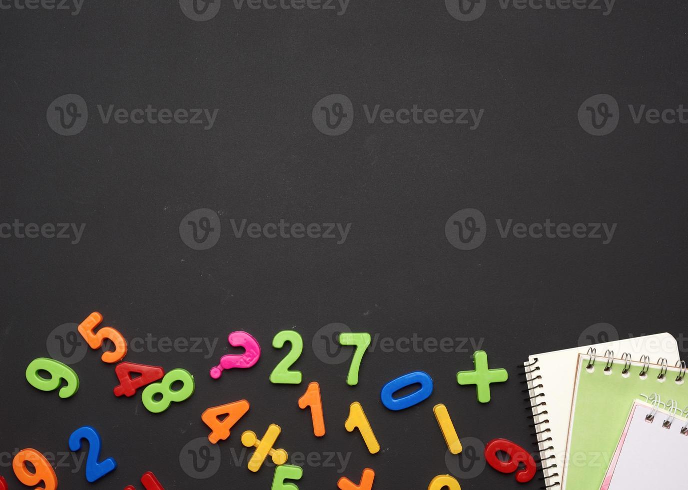 multicolored plastic numbers and a stack of notebooks on a black chalk board photo