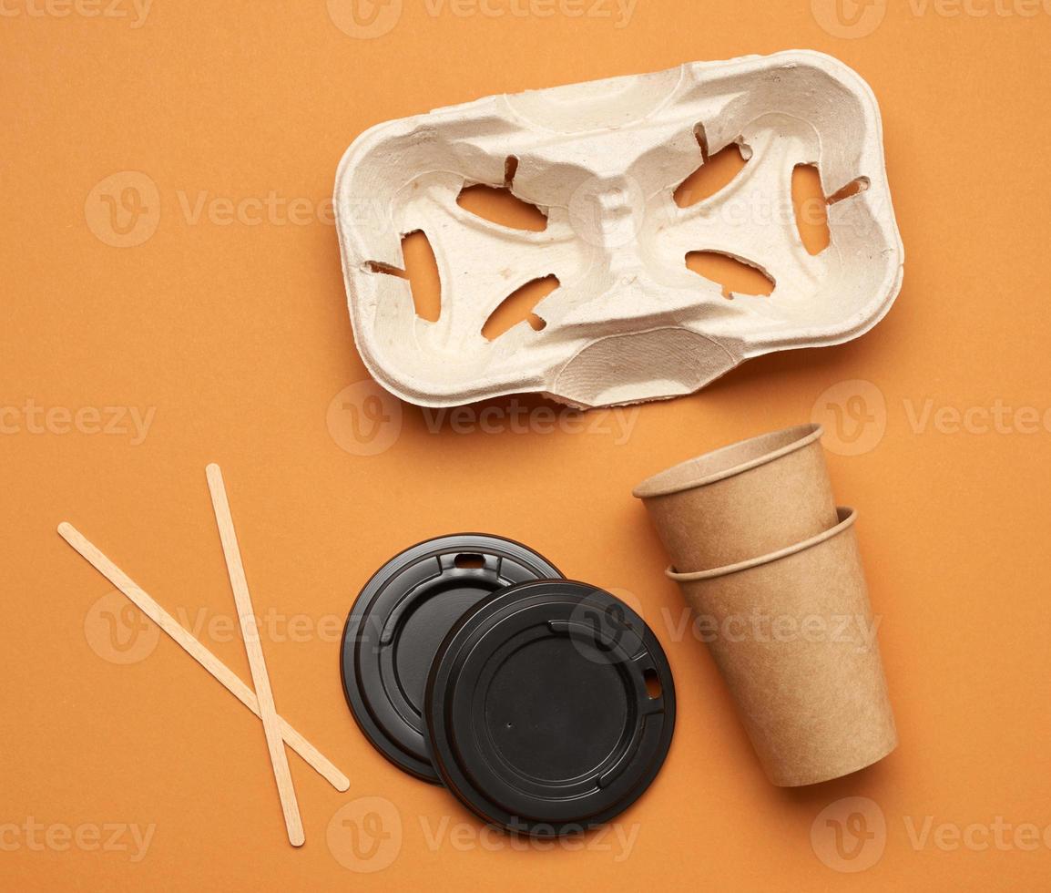 disposable paper cups from brown craft paper and recycled paper holders on a orange background photo