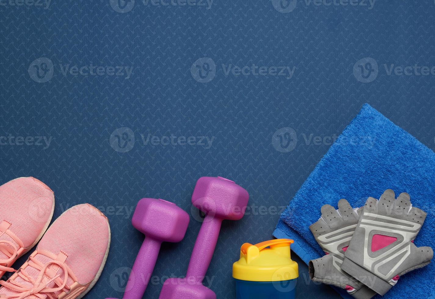 pair of purple dumbbells, sports gloves and pink gym shoes on a blue neoprene mat photo