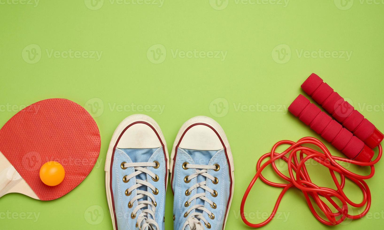 zapatillas de deporte, cuerda para saltar y raquetas de madera para tenis de mesa sobre un fondo verde foto