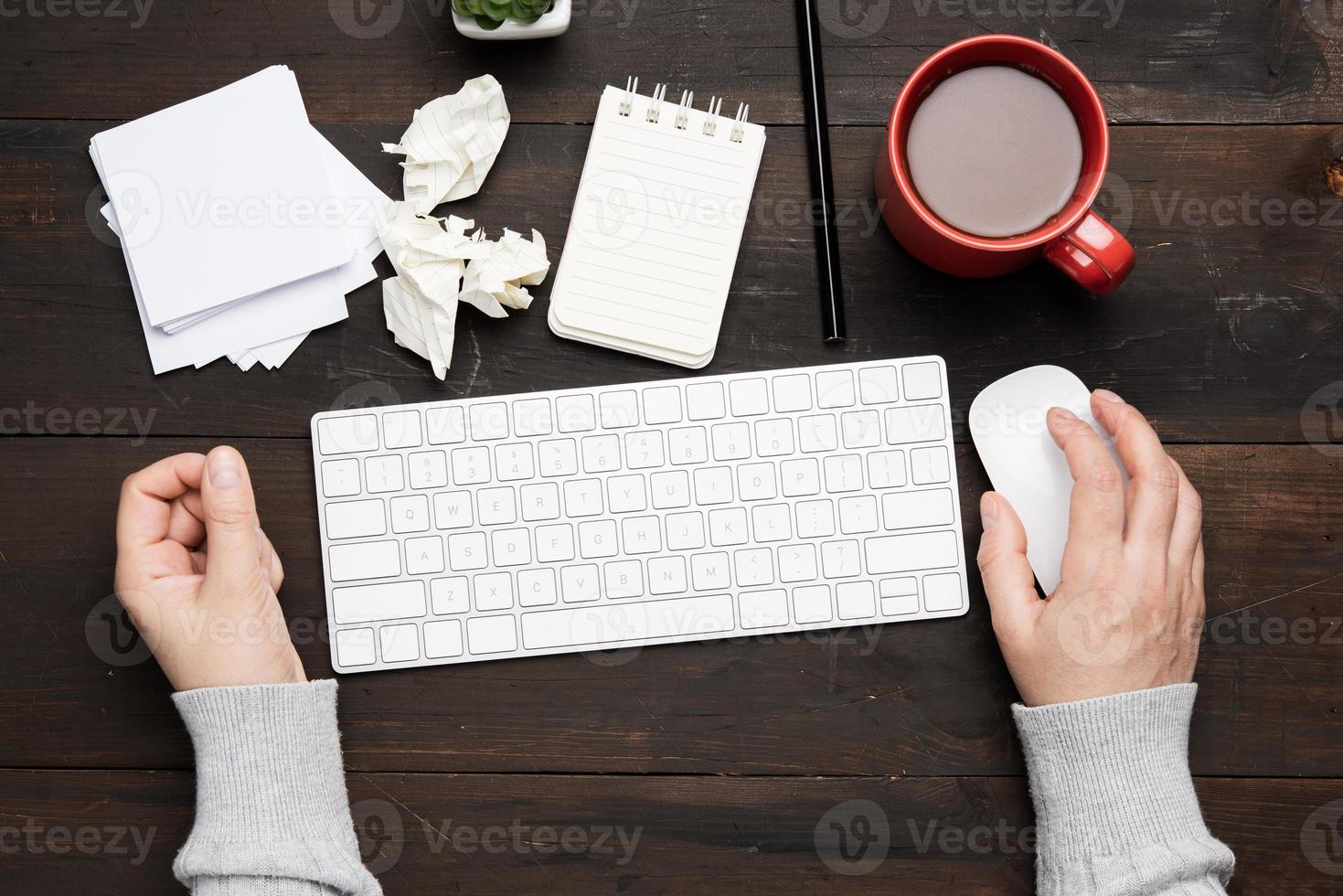 white wireless keyboard and mouse on a wooden brown table, next to a white cup with coffee photo