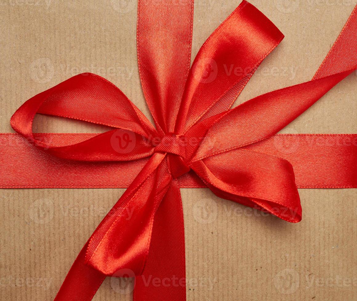 knotted bow made of red silk ribbon on brown kraft paper background photo