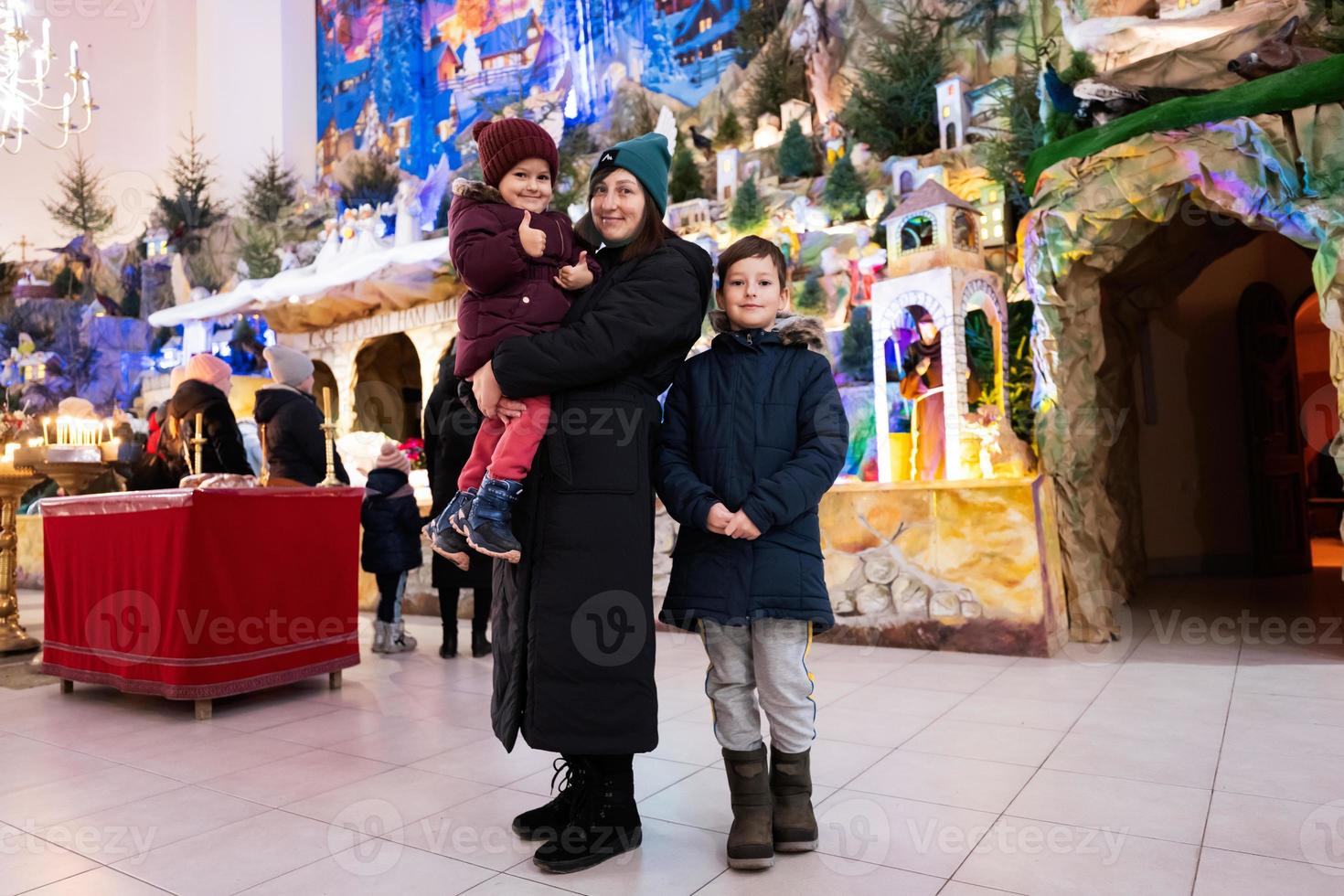 madre con hijos visita la escena del pesebre navideño en la iglesia. foto