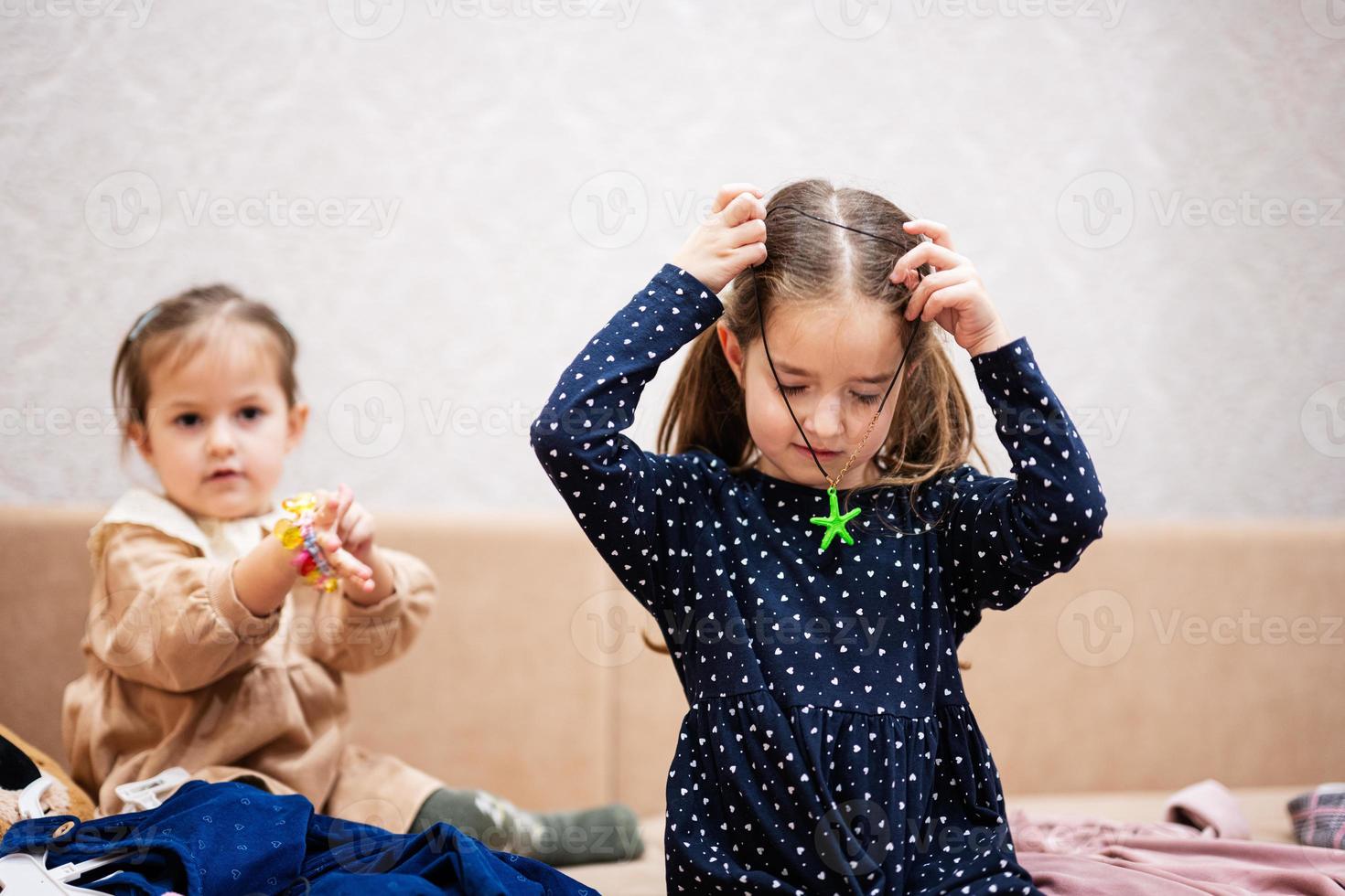 dos hermanas están eligiendo ropa del armario en casa en el sofá. la niña lleva un colgante de estrella de mar alrededor de su cuello. foto