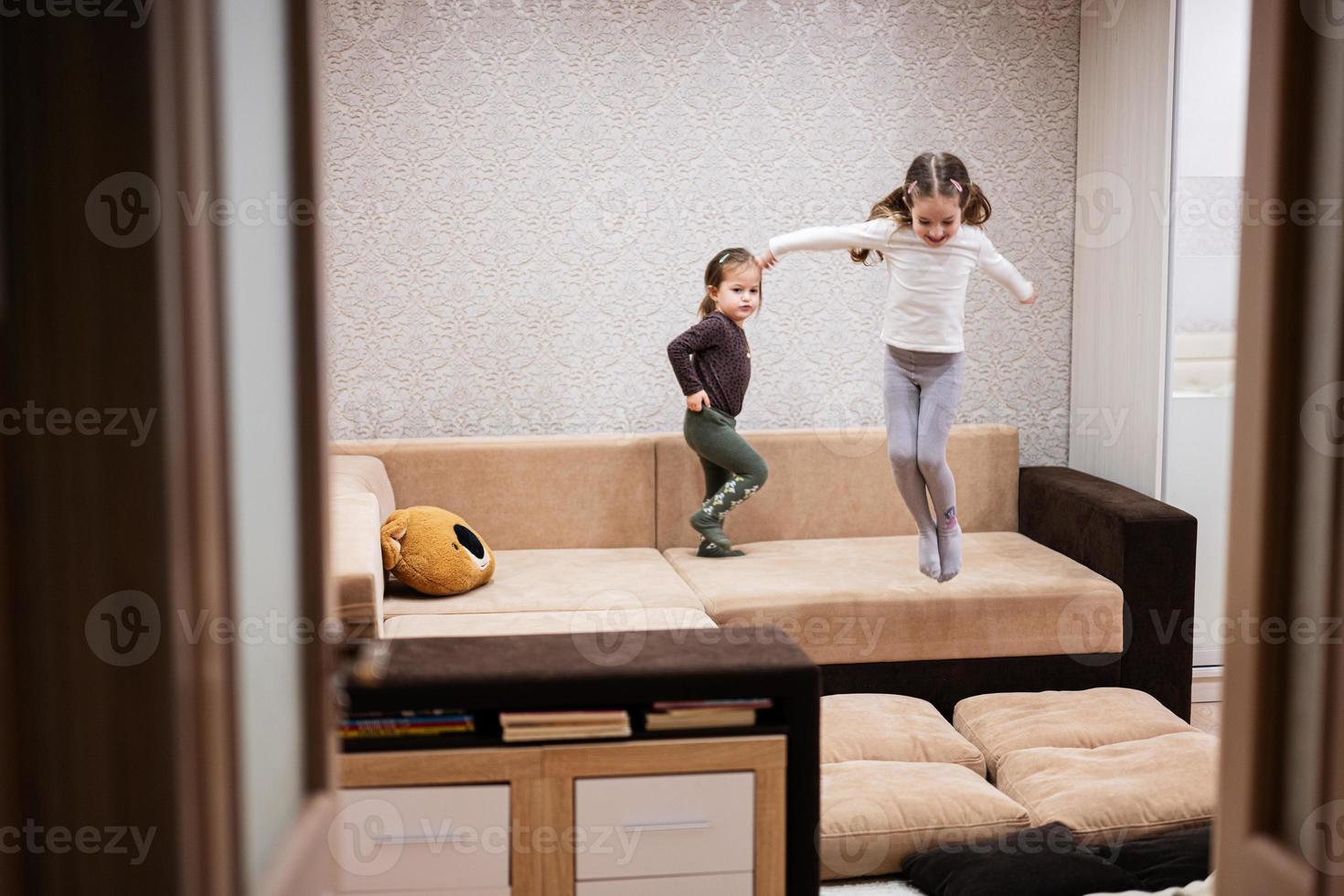 Two sisters at home on the sofa jumping together. photo