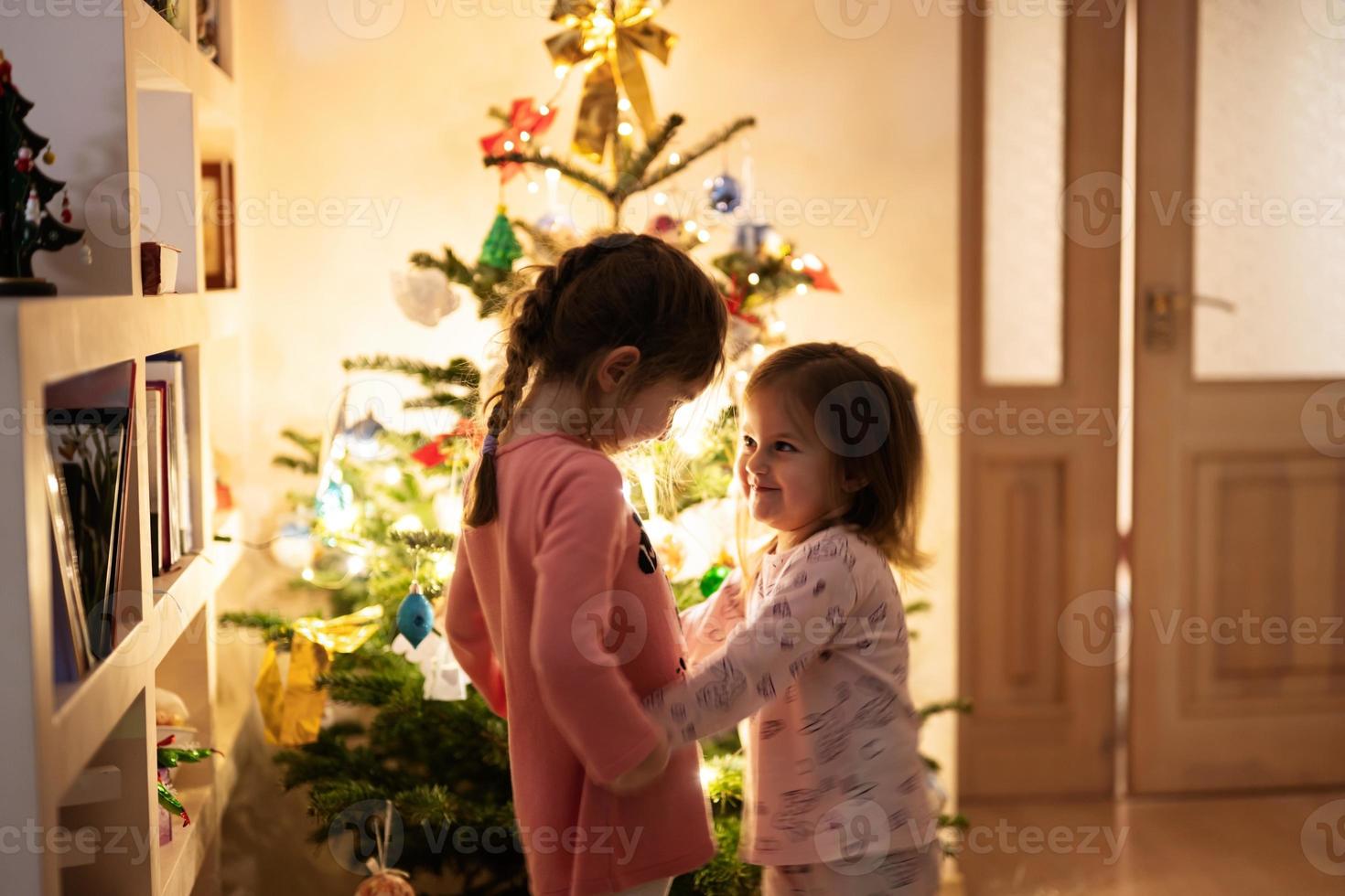 Two sisters together near Christmas tree at evening home. photo