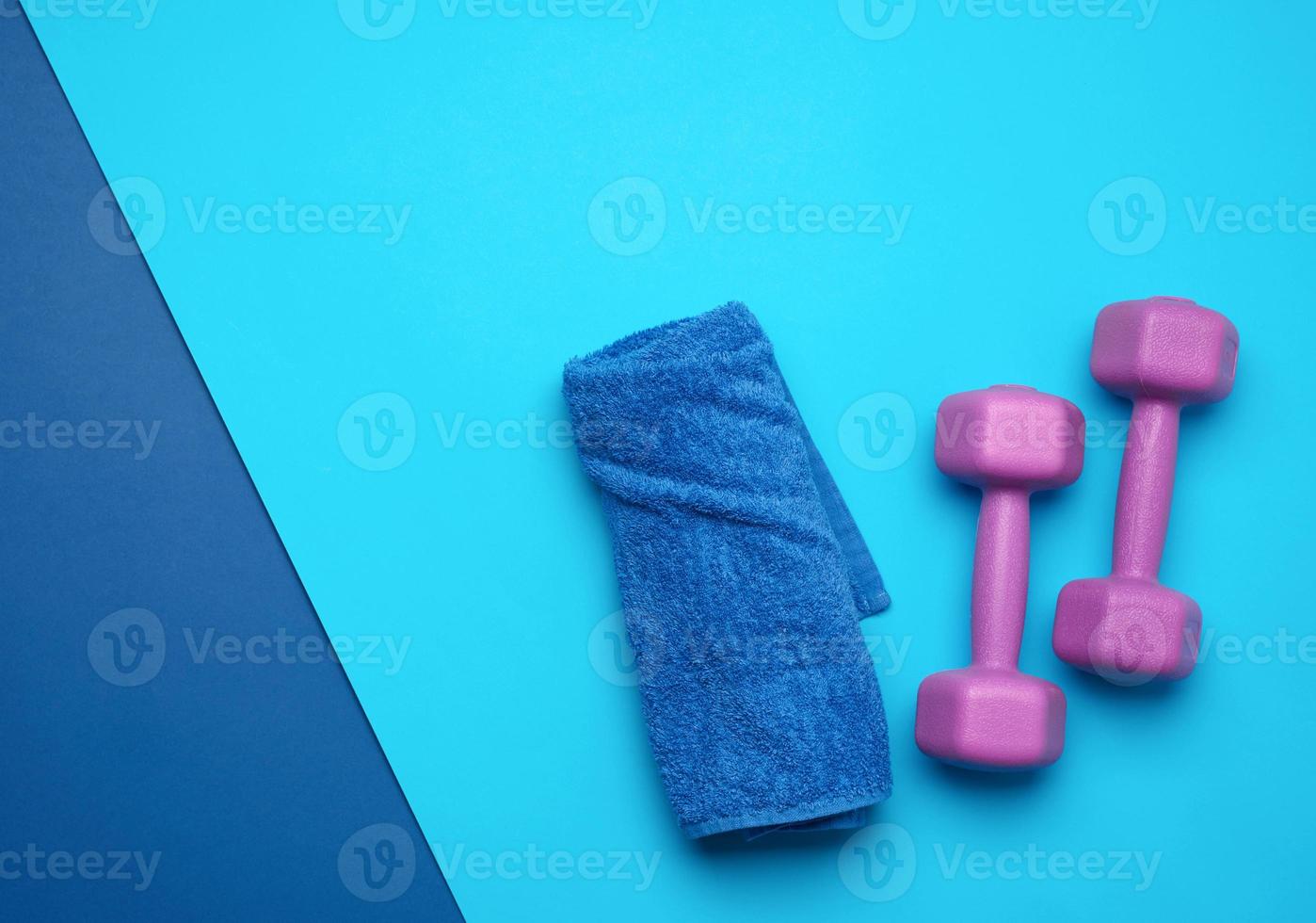 pair of purple dumbbells and blue towel on a blue background photo