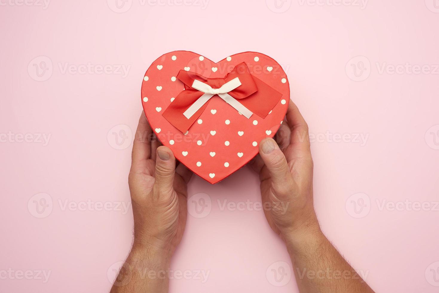 male hand holding a red cardboard box with a bow photo