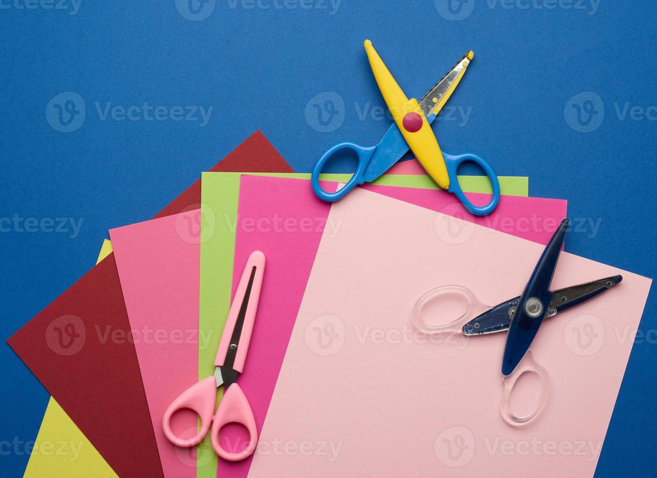 multicolored craft paper and plastic scissors on blue background photo