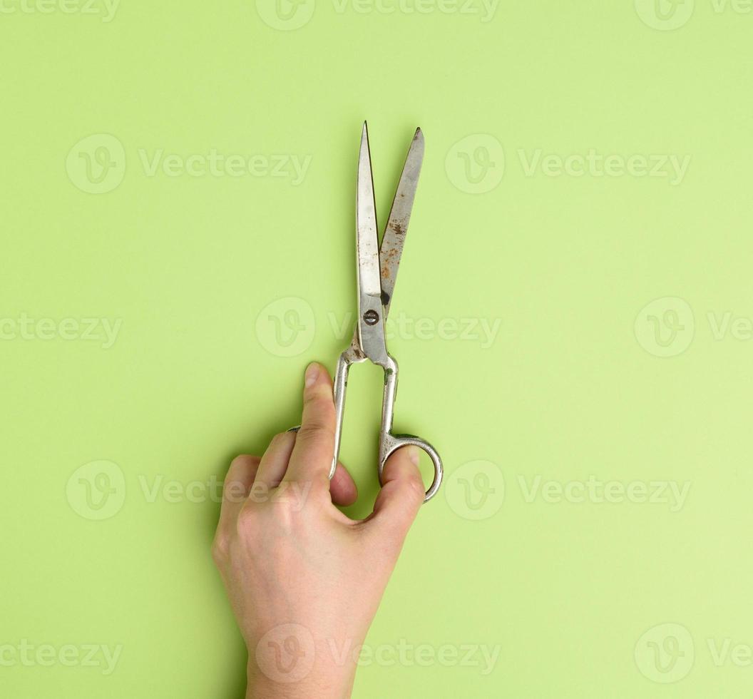 hand holds metal scissors on green background photo