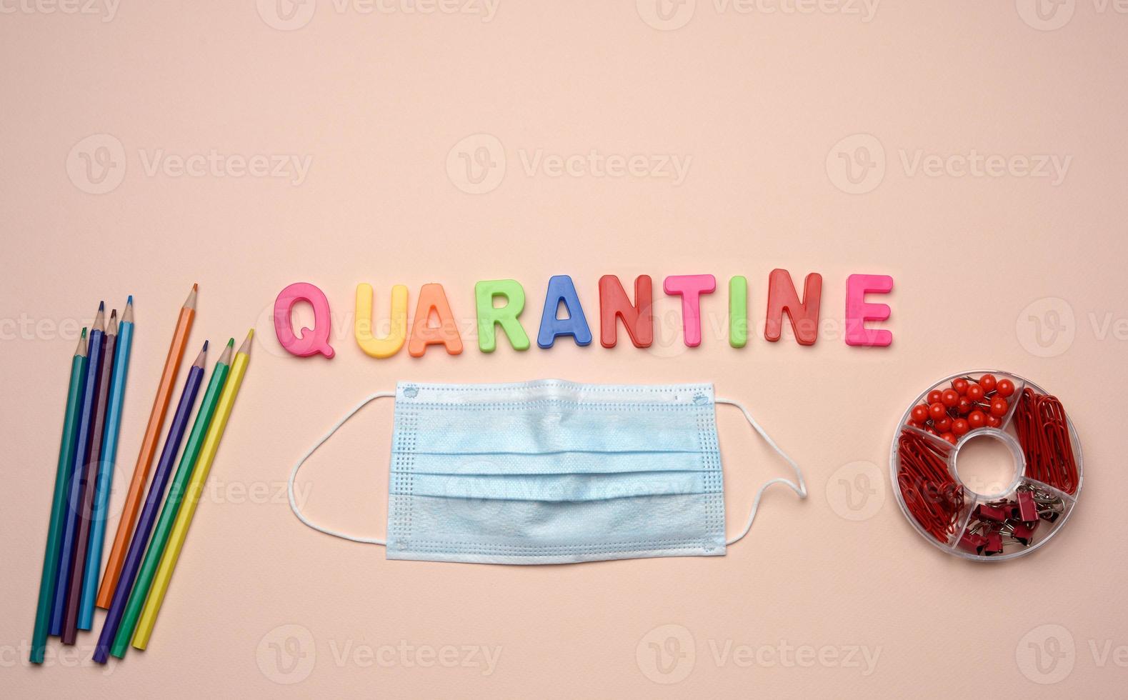 disposable medical mask and the inscription quarantine from plastic multicolored letters on a beige background, top view photo