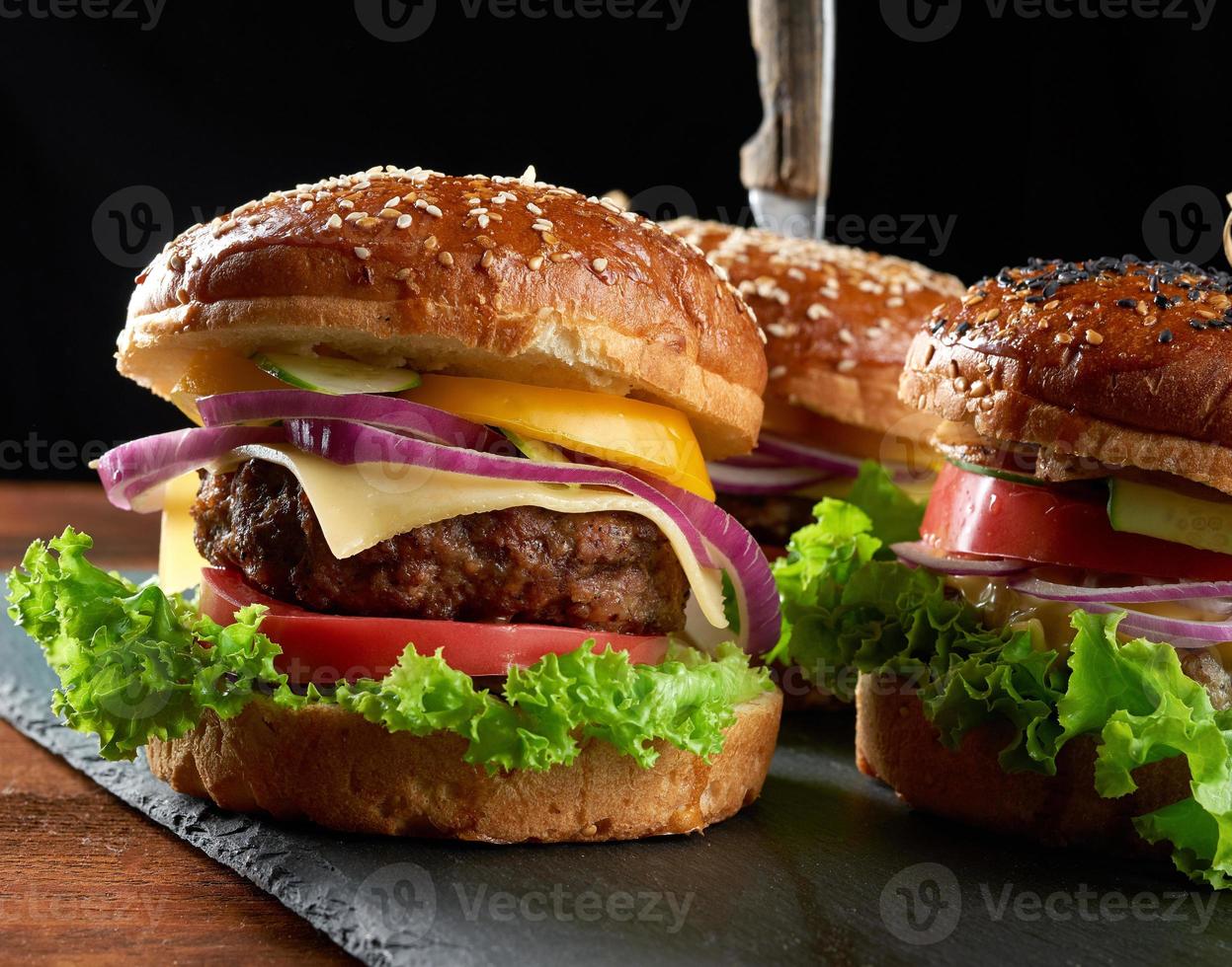 deliciosas hamburguesas con chuleta de ternera frita, tomate, lechuga y cebolla, bollo de harina de trigo blanco crujiente con semillas de sésamo foto