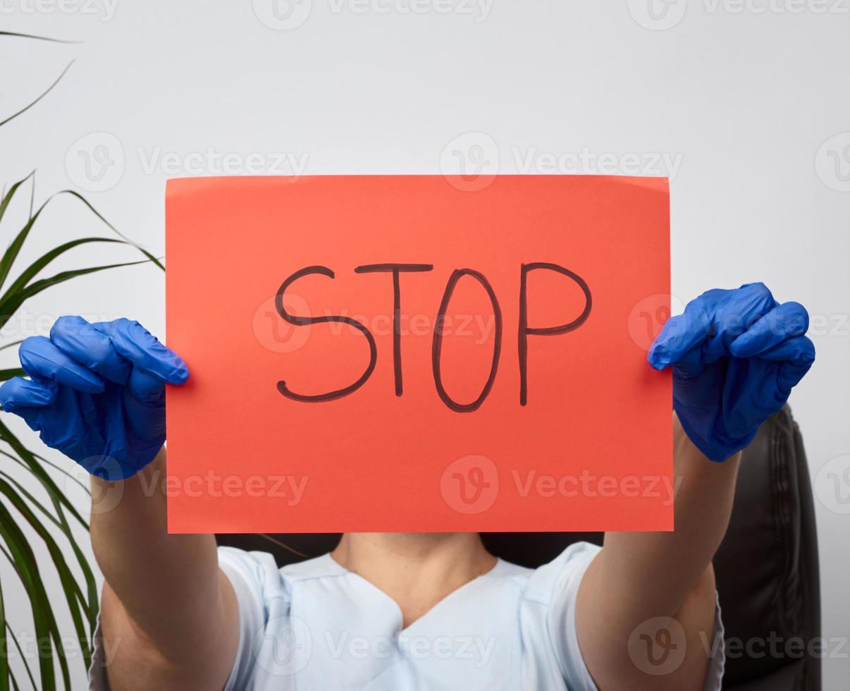 female medic is sitting in a brown leather chair in the office holding a red sheet of paper with the words stop photo