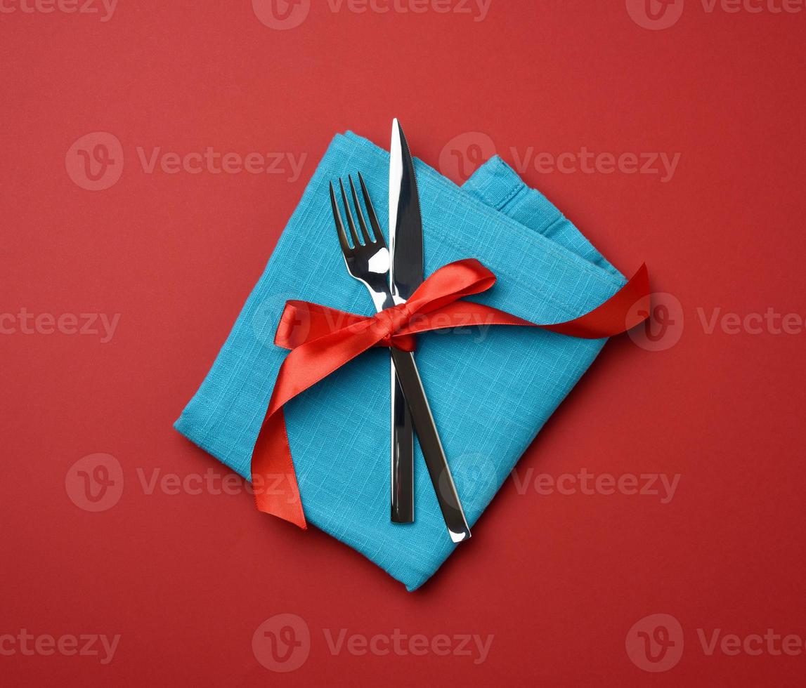 metal fork and knife tied with a red silk ribbon, red background photo