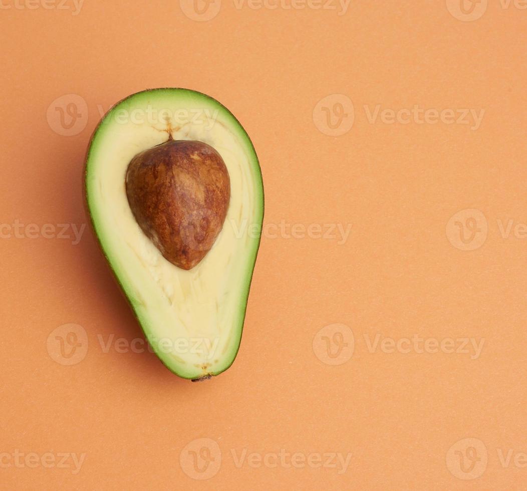 aguacate verde medio maduro con un hueso marrón sobre un fondo naranja abstracto foto