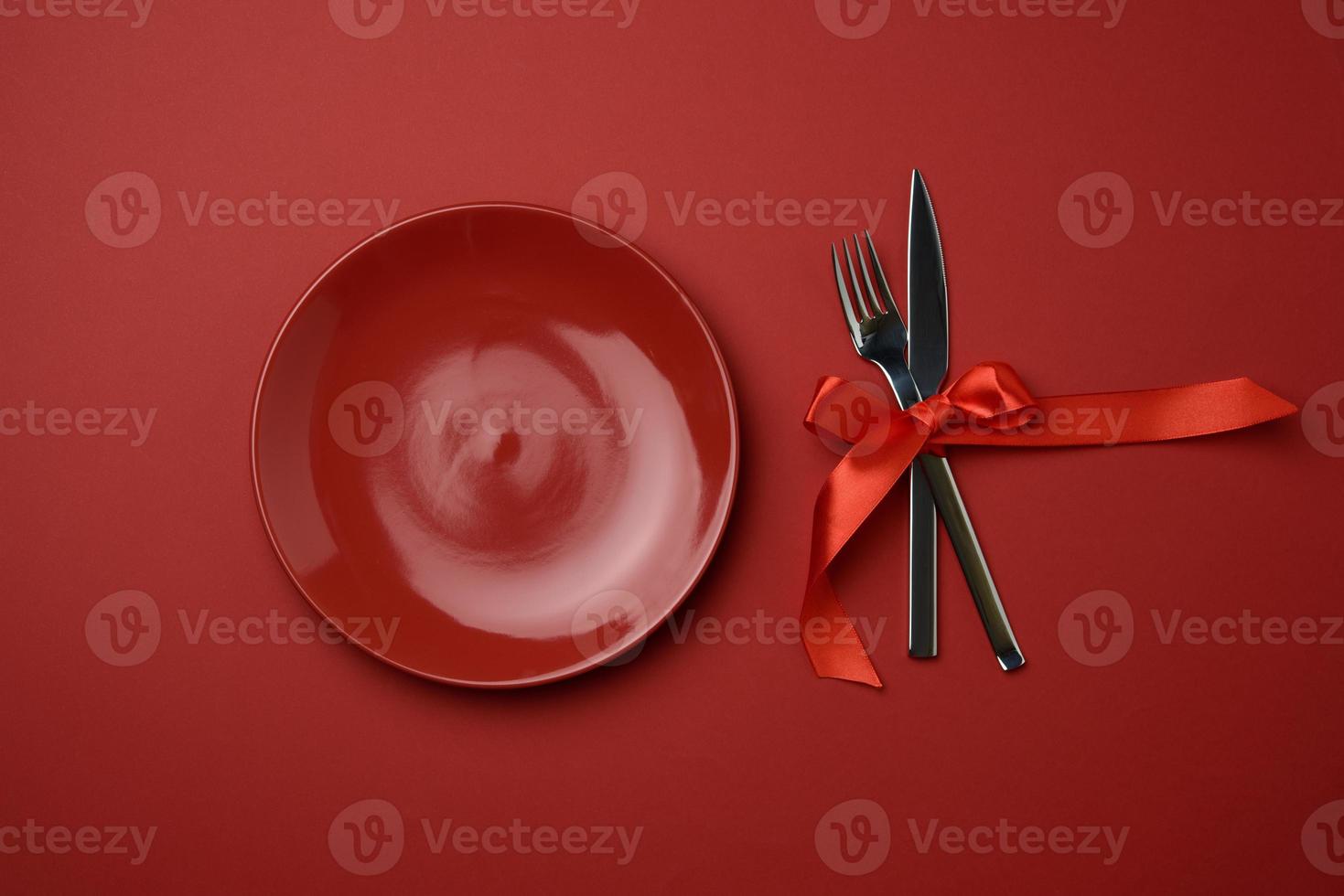 red round empty ceramic plate and metal fork and knife tied with a red silk ribbon photo