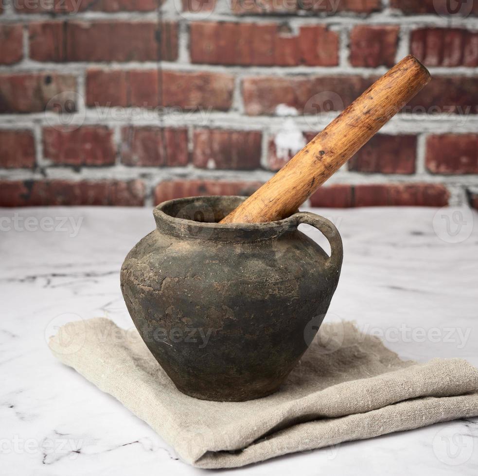 olla de barro negro y mano de mortero de madera sobre fondo de pared de ladrillo marrón foto