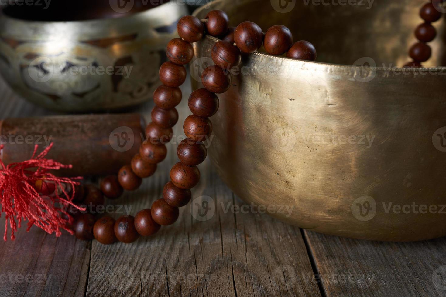 Tibetan singing copper bowl with a wooden clapper and prayer rosary on a gray wooden table photo