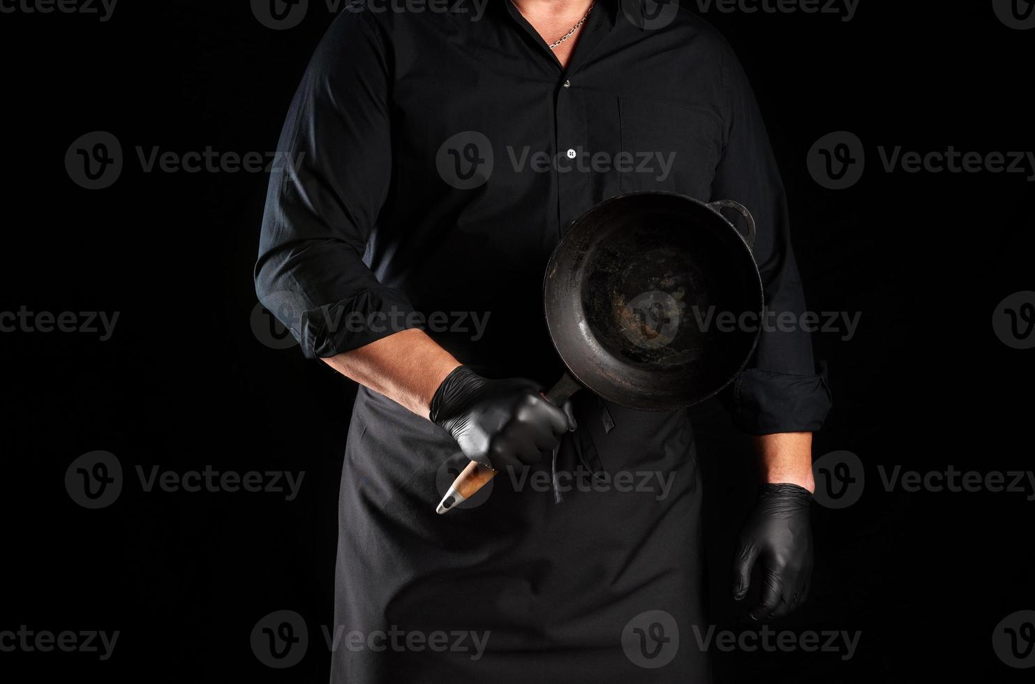 male cook in black uniform and latex gloves holds an empty round vintage black cast iron pan photo