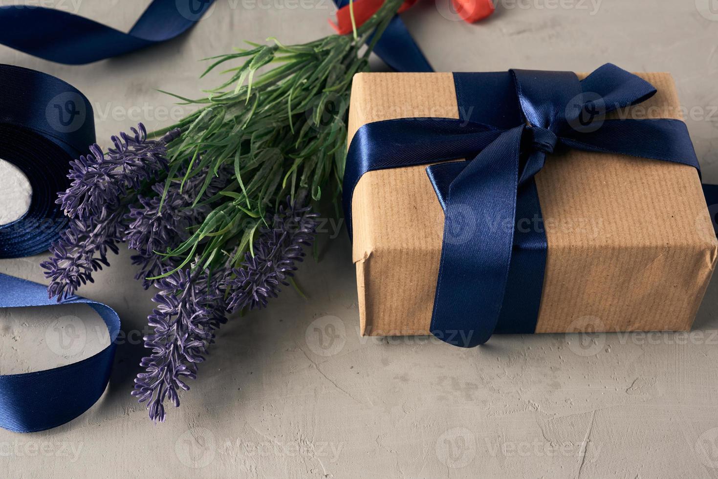 regalo envuelto en papel kraft marrón y atado con un lazo de seda azul, mesa gris foto