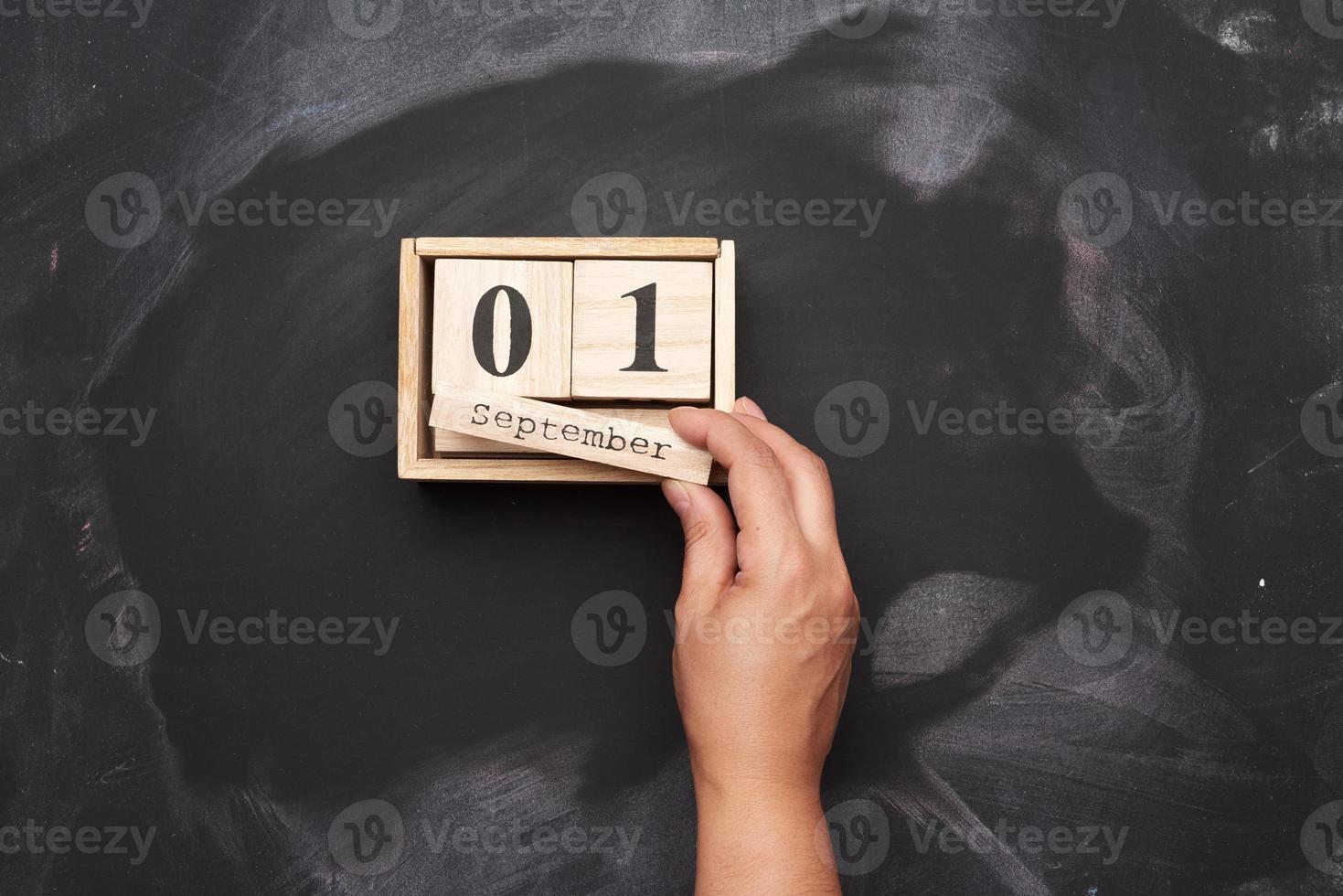 wooden calendar with date 1st september and female hand, black chalk board background photo