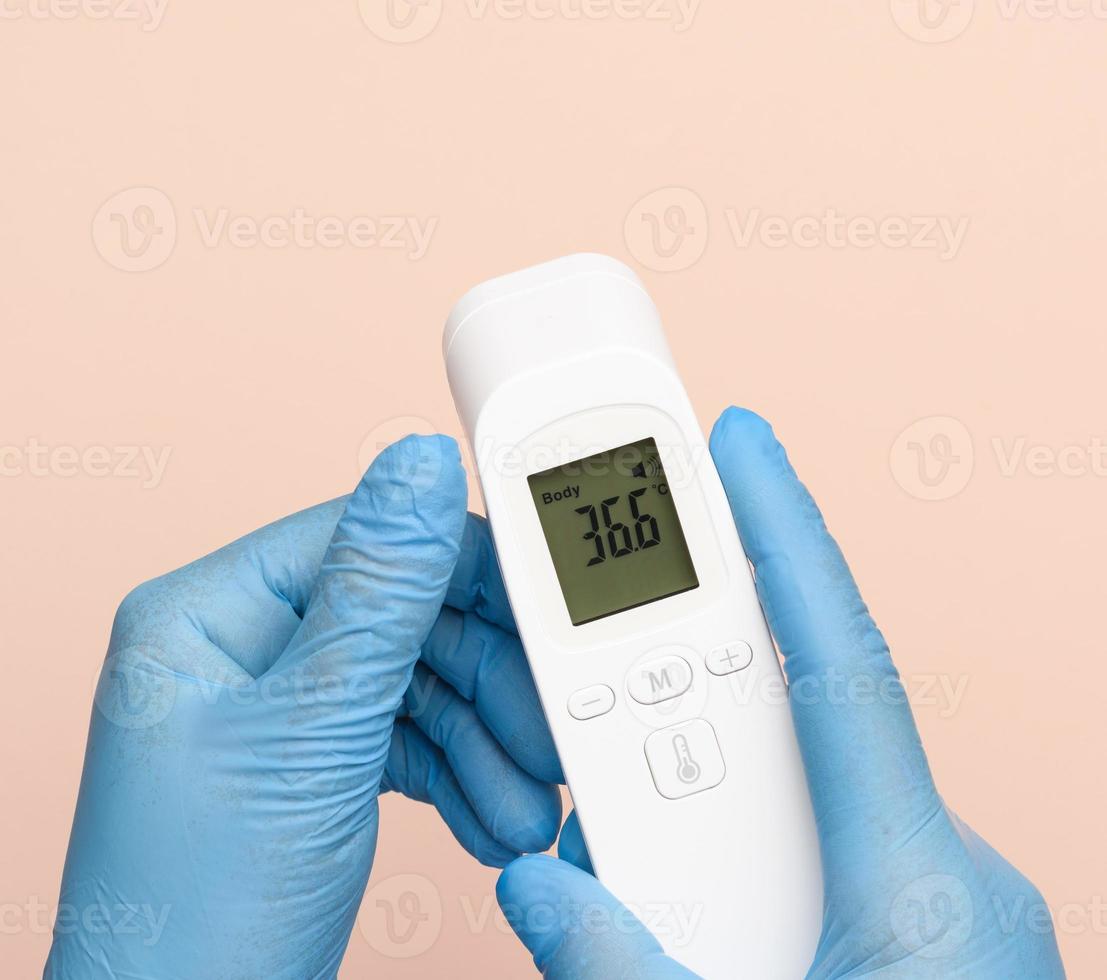 hand in blue latex gloves hold an electronic thermometer to measure temperature photo