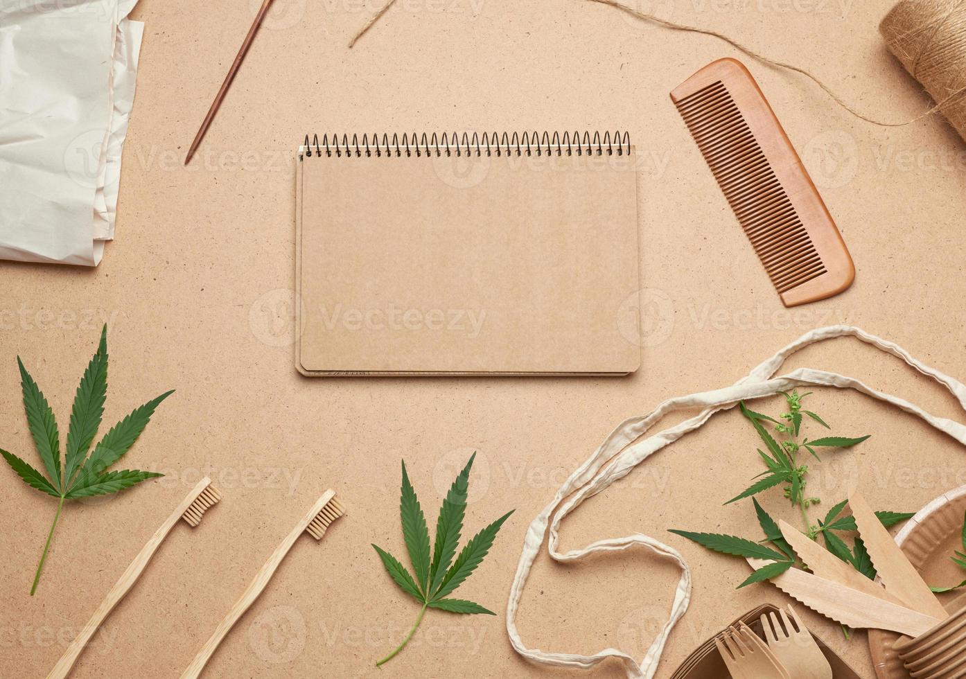 open notebook with empty sheets, a textile bag and disposable tableware from brown craft paper, green hemp leaves photo