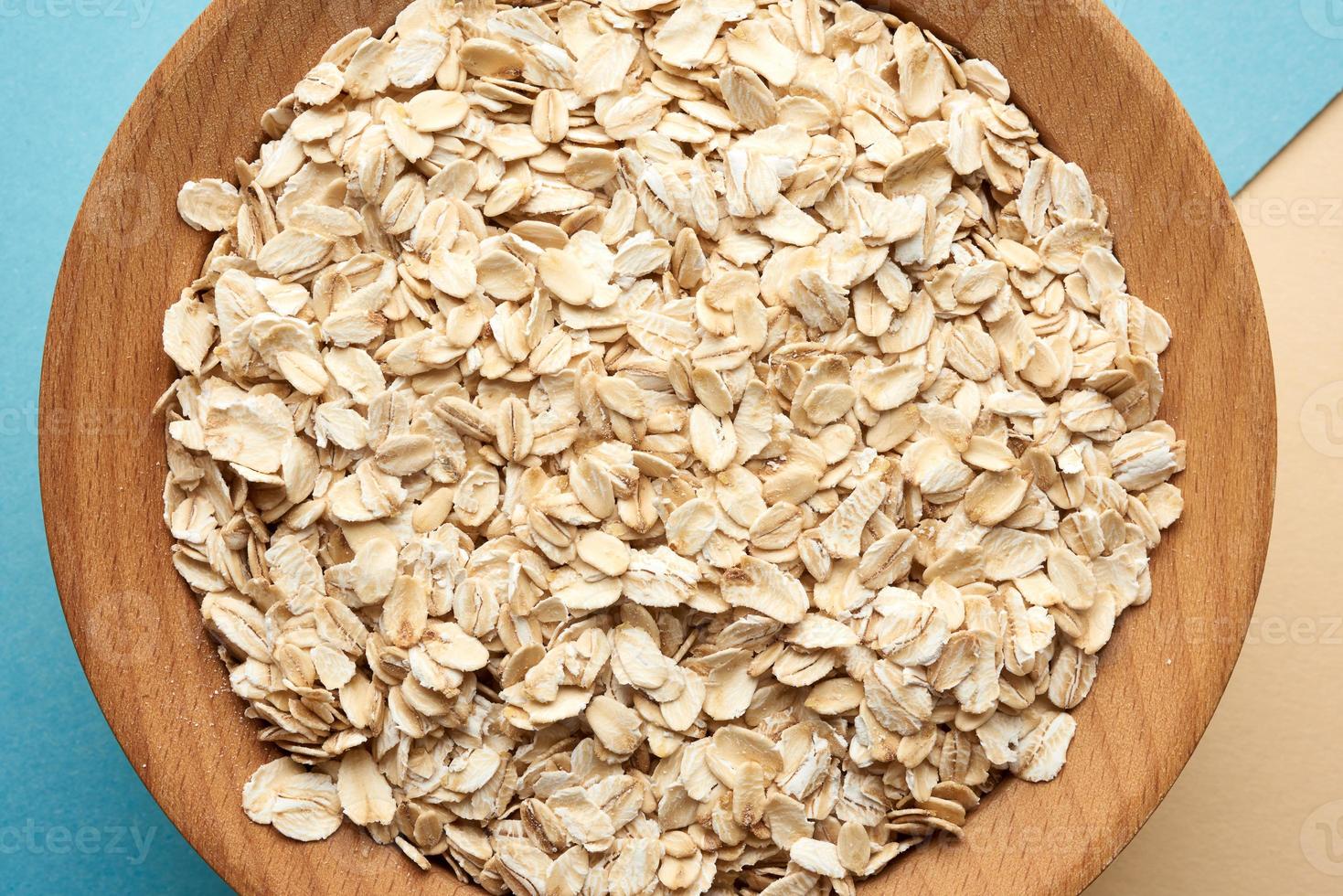 avena cruda en un cuenco de madera marrón sobre un fondo azul foto