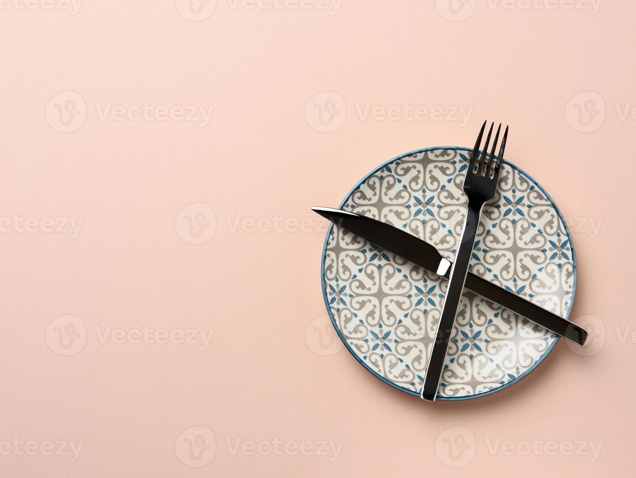 round ceramic plate and crossed knife and fork on beige background photo