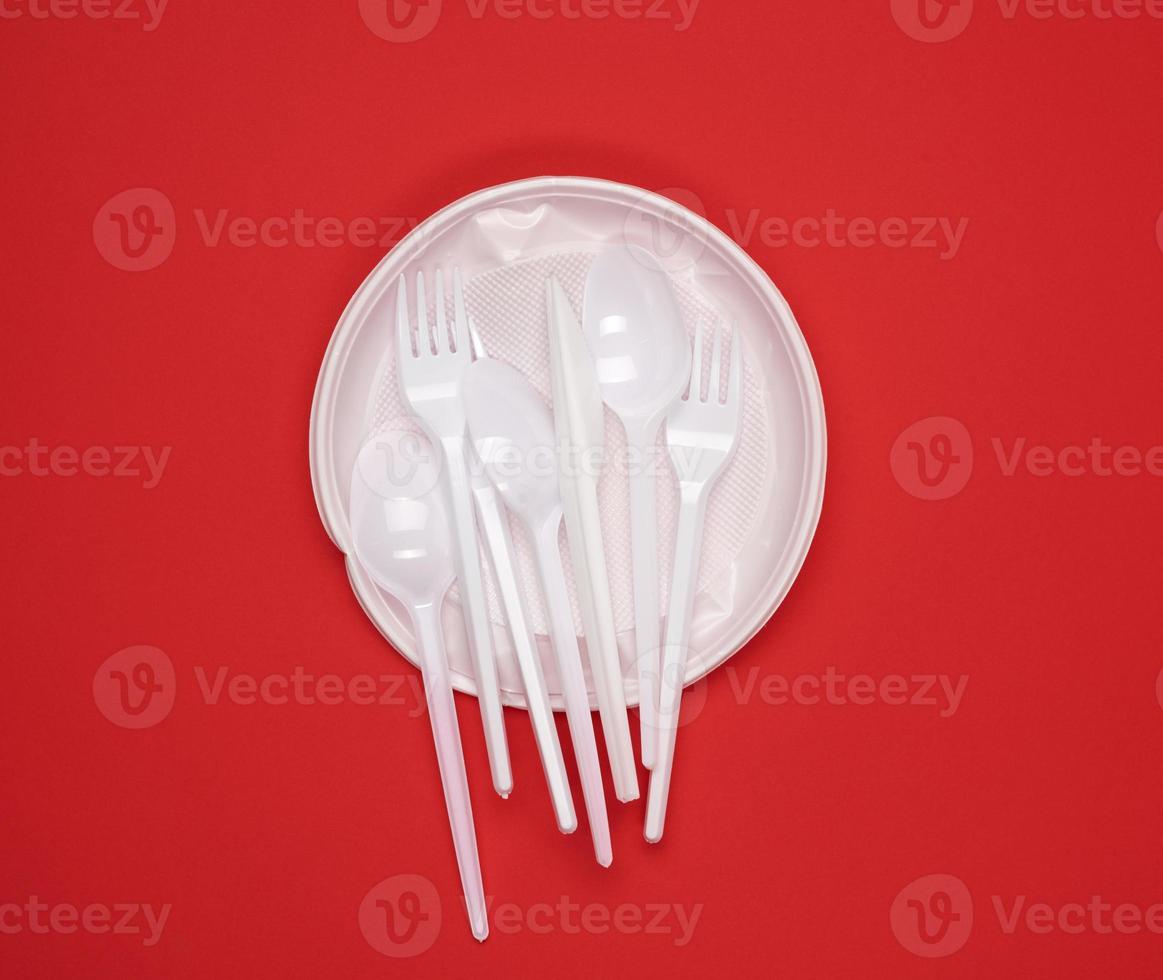 round plate and stack of plastic forks and spoons on red background photo