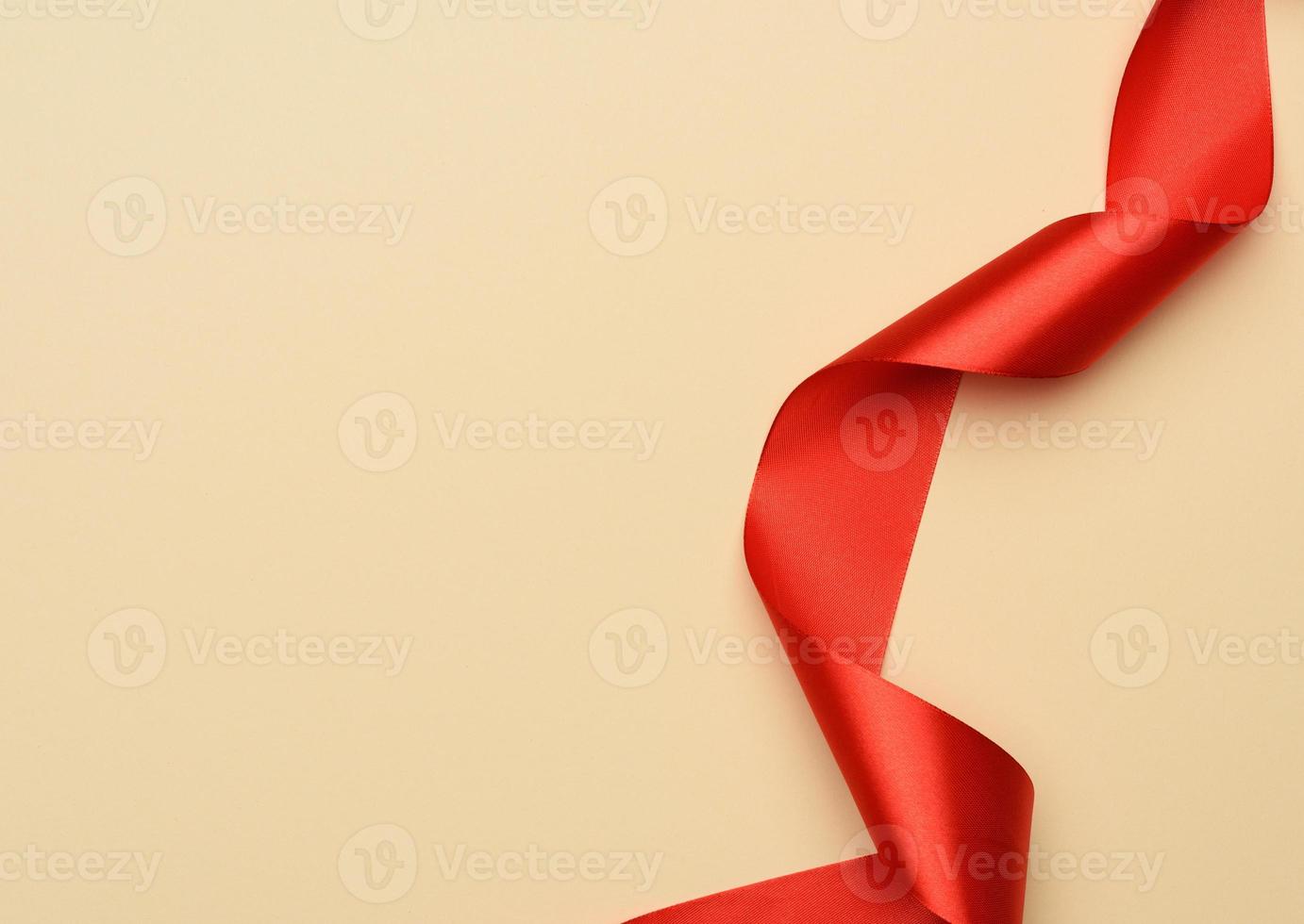 curled red silk ribbon on a beige background photo